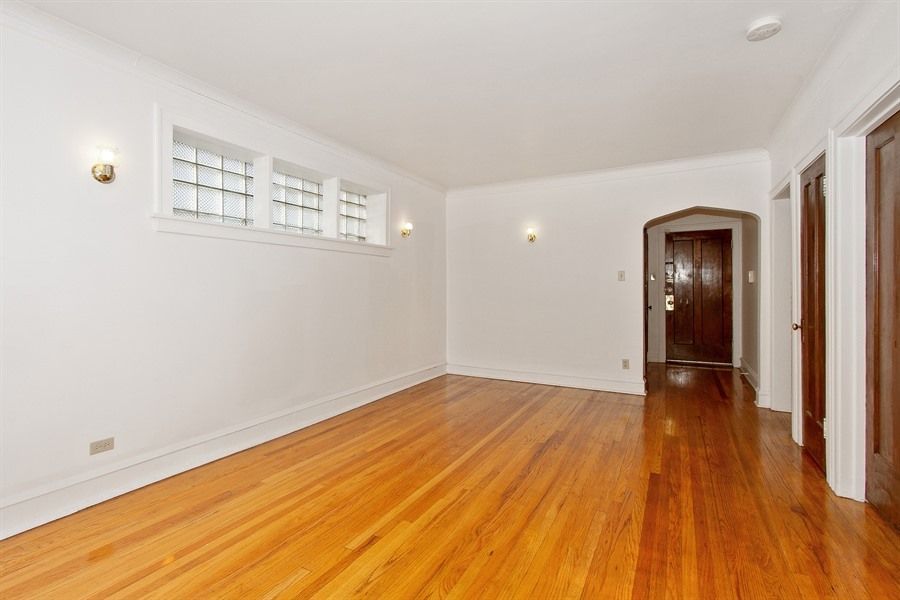 Empty room with hardwood floors, white walls, arched doorway, and decorative lighting.