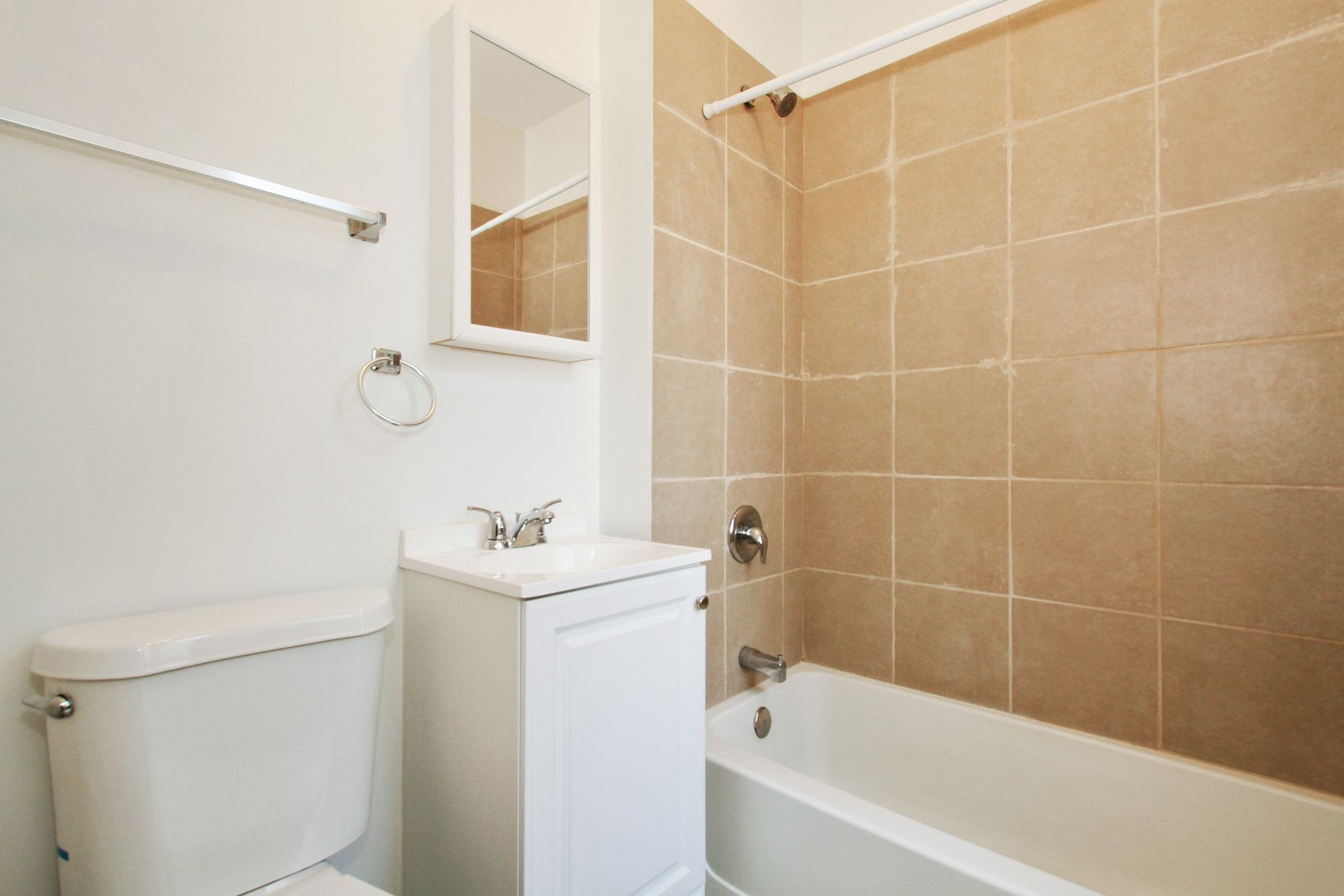 Bathroom with white fixtures, beige tiled shower/tub, and a mirror.
