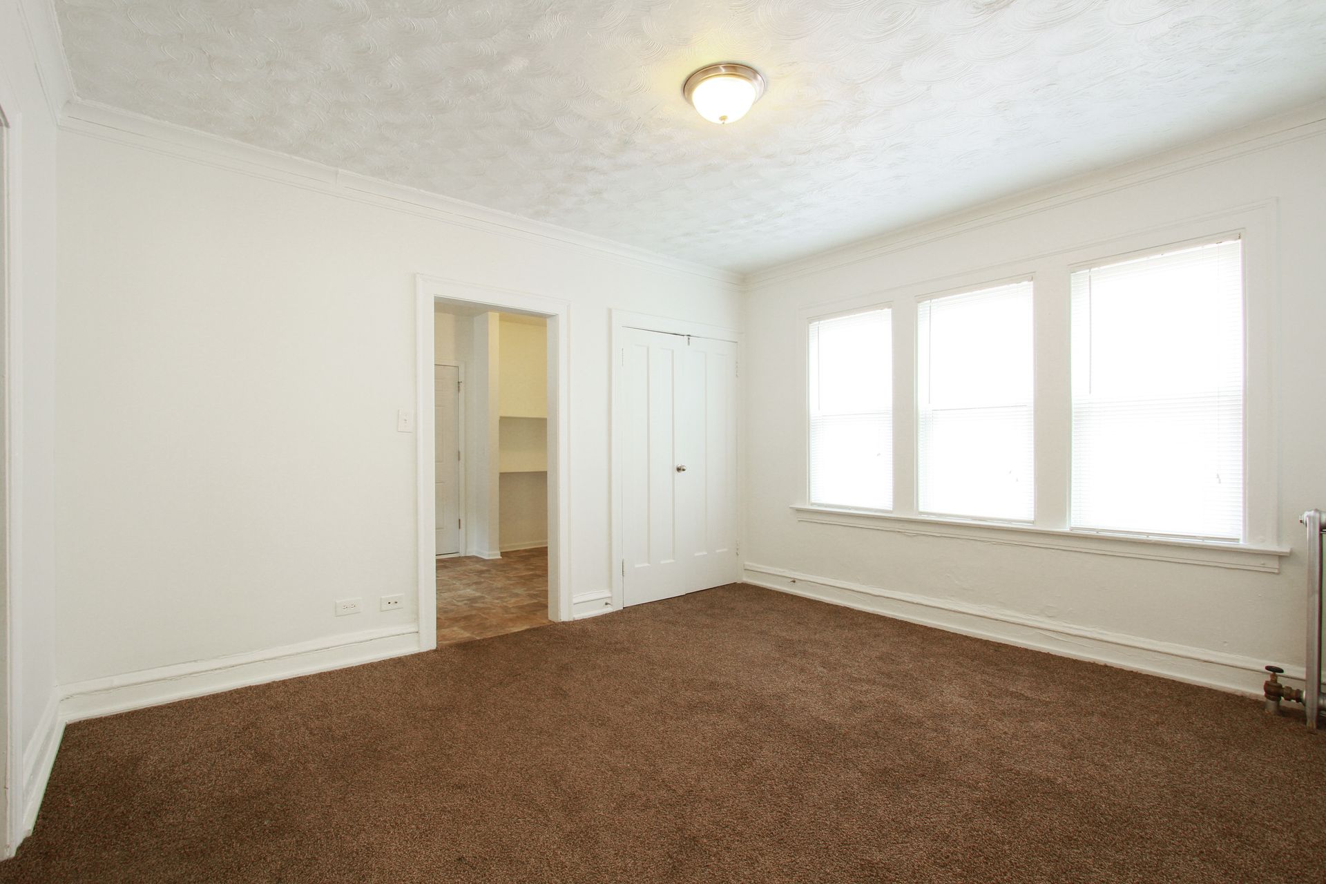 Empty room with brown carpet, white walls, and a three-window view.