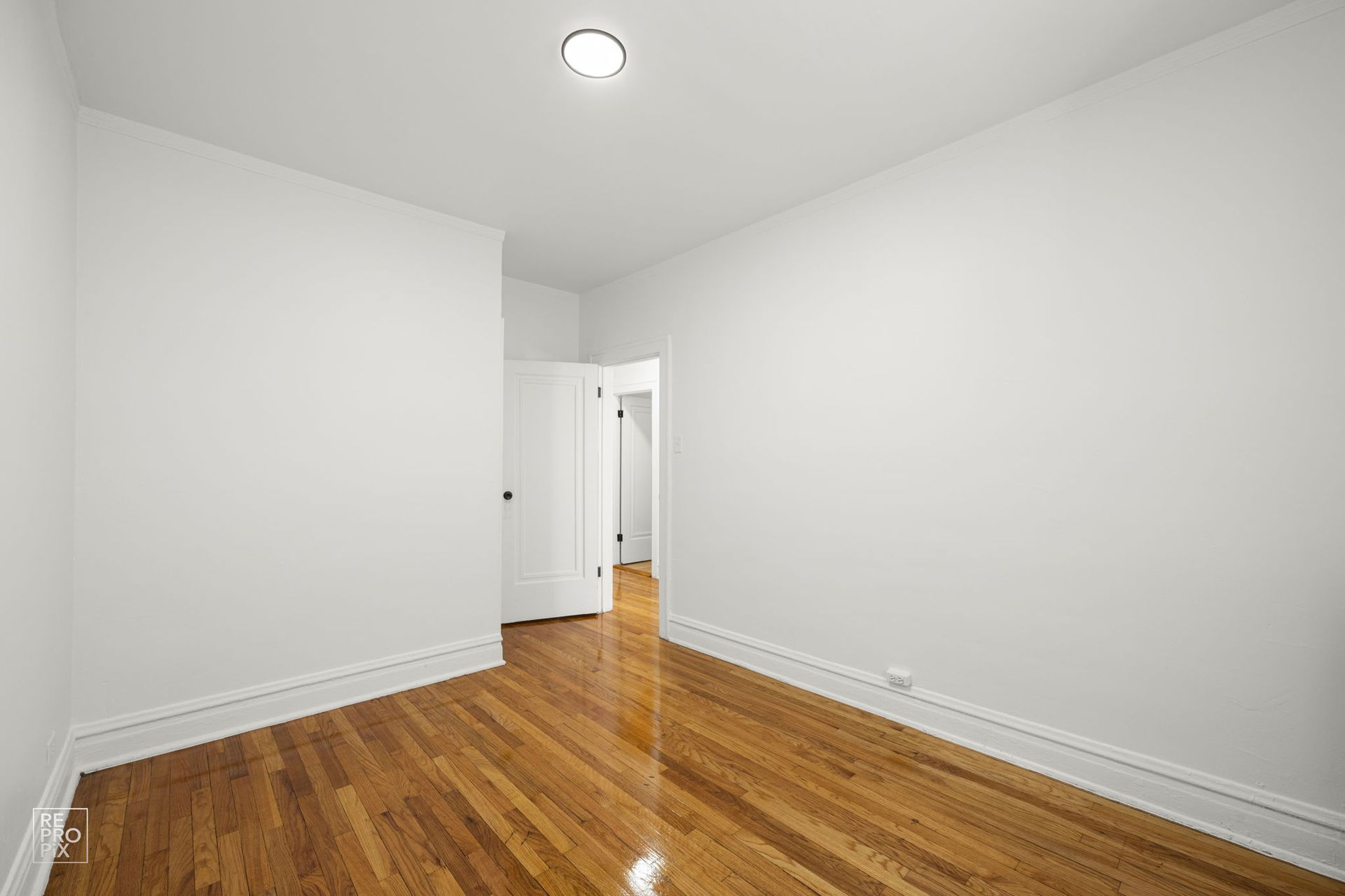 Empty room with hardwood floors, white walls, and a doorway leading to another room.