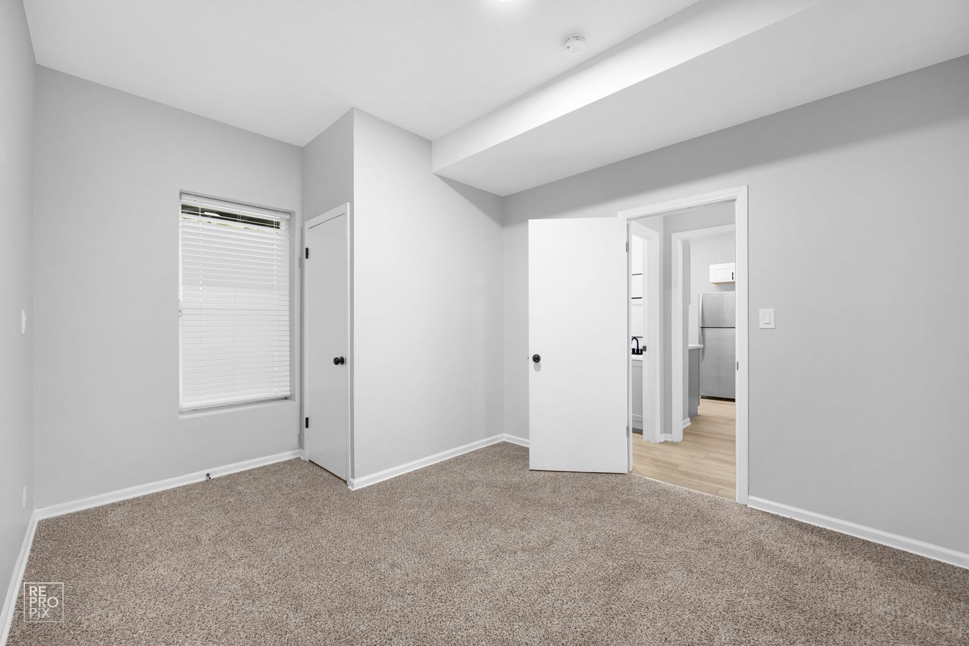 Empty gray bedroom with carpet, a window, and doors leading to other rooms.