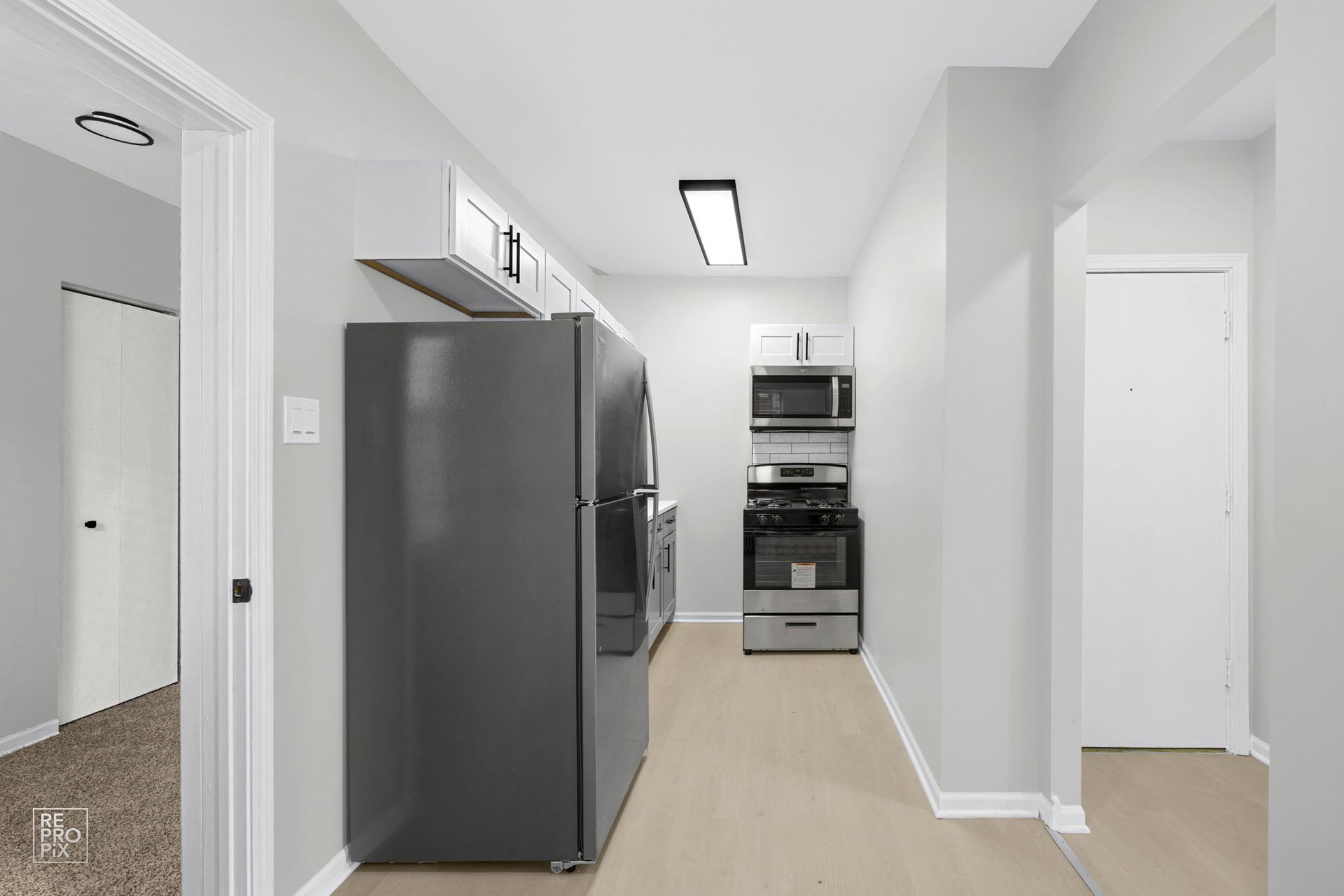 Narrow kitchen with gray appliances and light wood floors.