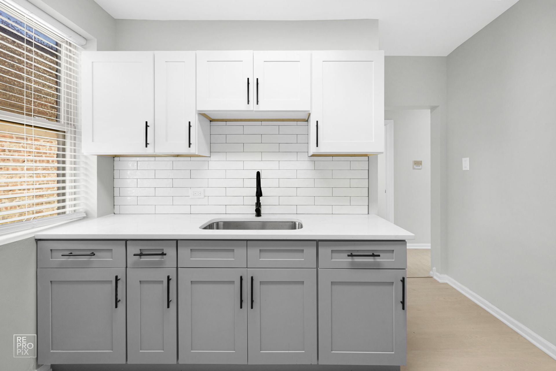 Kitchen with white and gray cabinets, subway tile backsplash, and a window with blinds.