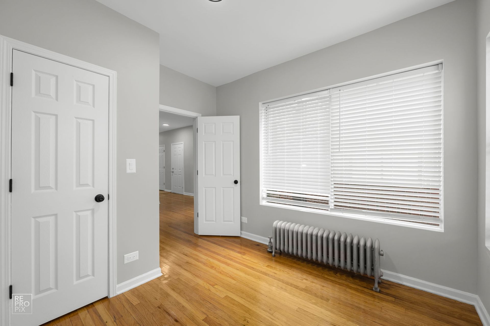 Empty room with hardwood floors, a closed white door, and a window with blinds.