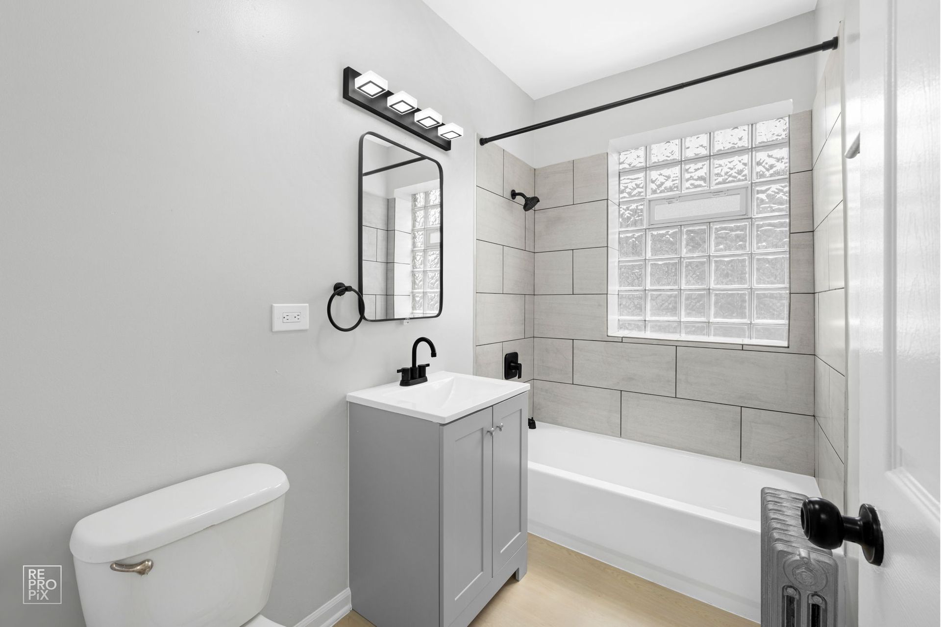 Gray bathroom with toilet, vanity, and shower/tub. Gray and white tiles, black fixtures.
