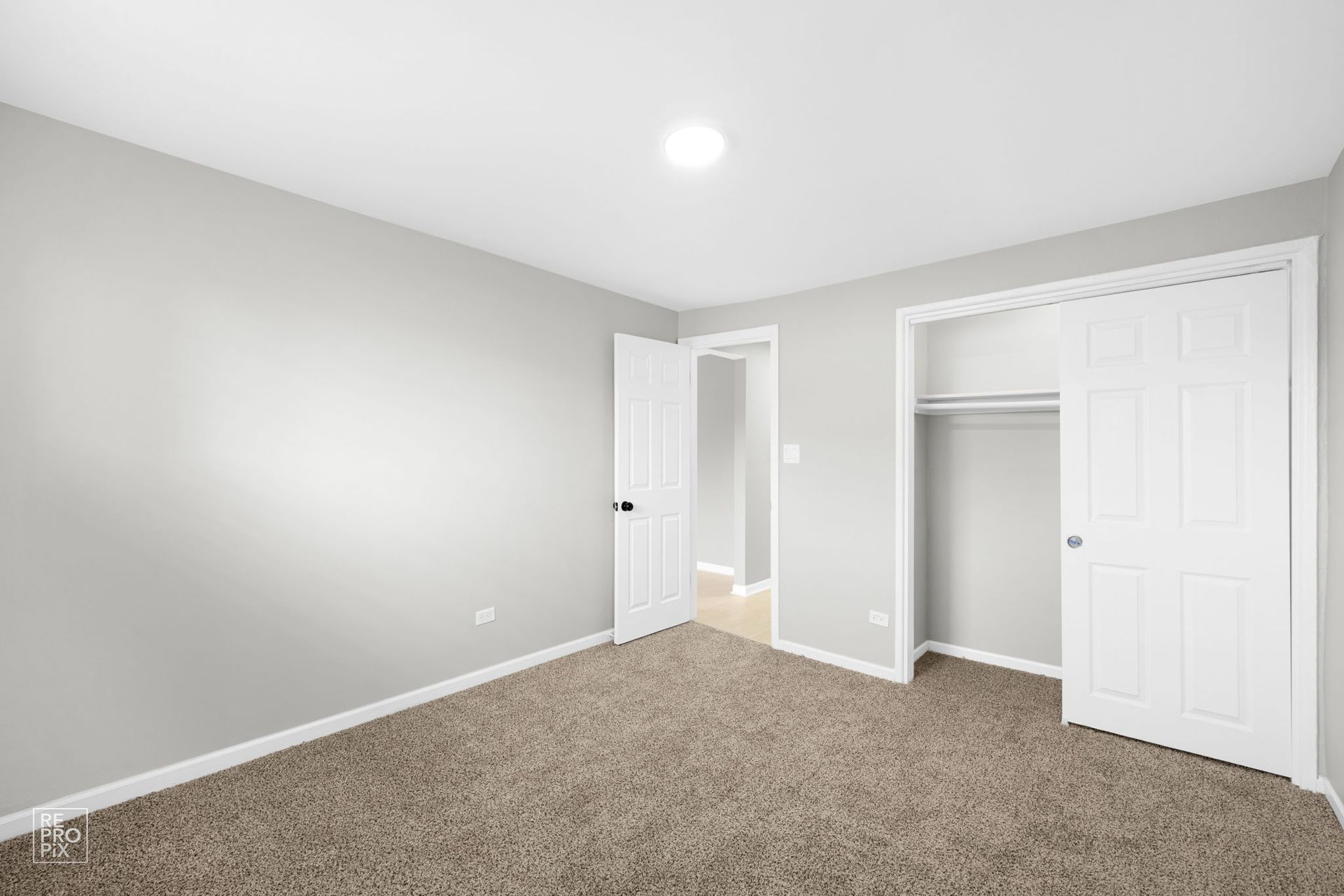Three-story brick apartment building with brown trim under a blue sky, surrounded by green shrubs and trees.