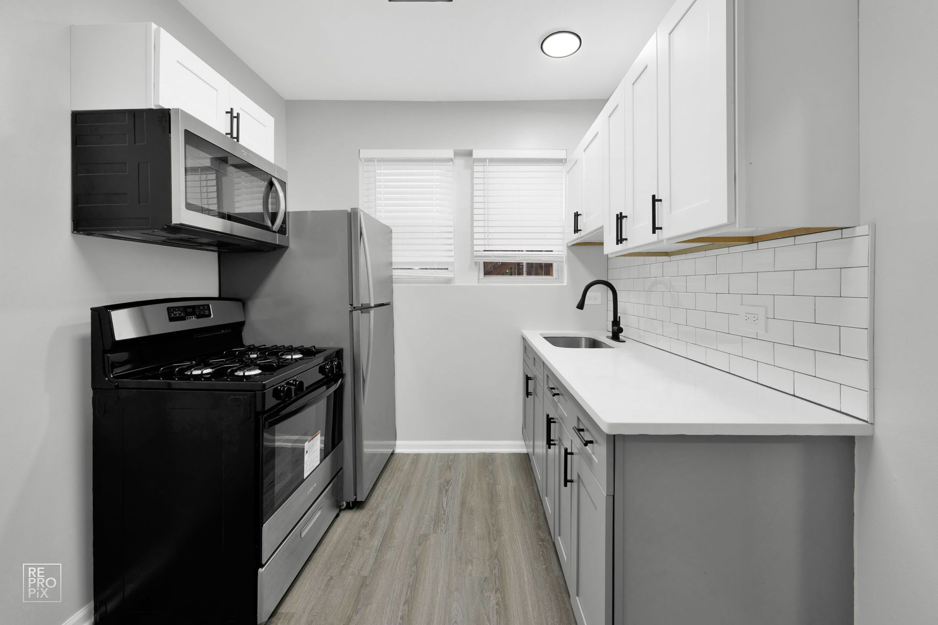 Small kitchen with gray cabinets, white countertops, stainless steel appliances, and a window.