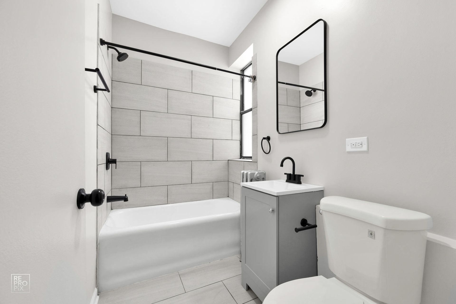 Bathroom with white tile, a gray vanity, black fixtures, and a toilet.