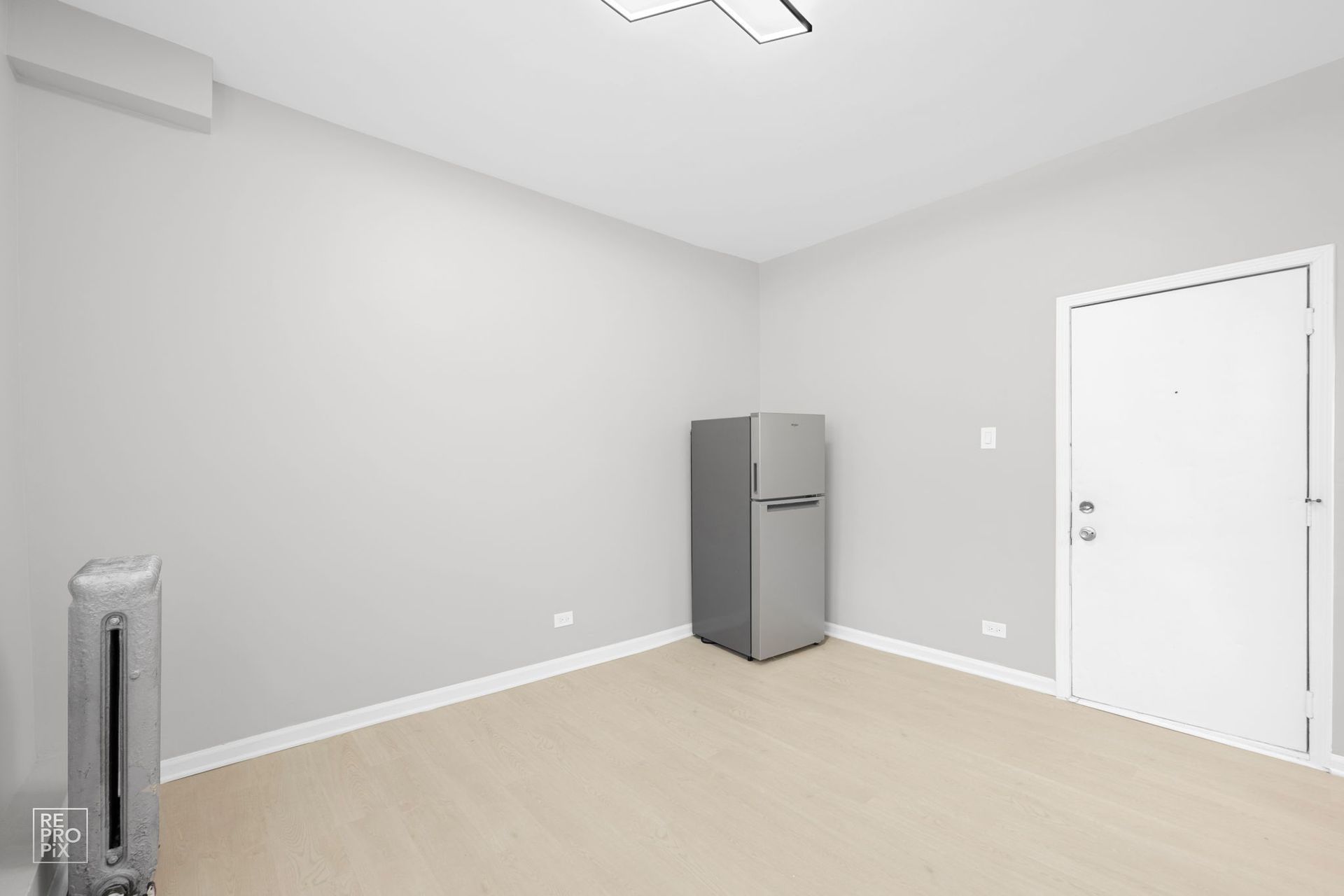 Empty room with gray walls, refrigerator, heater, and a white door.