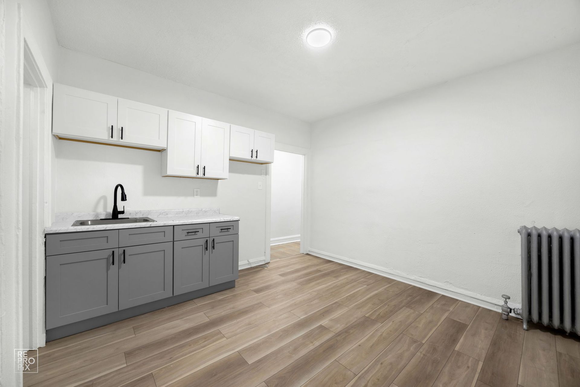 Empty kitchen with white and gray cabinets, sink, and wooden floor.