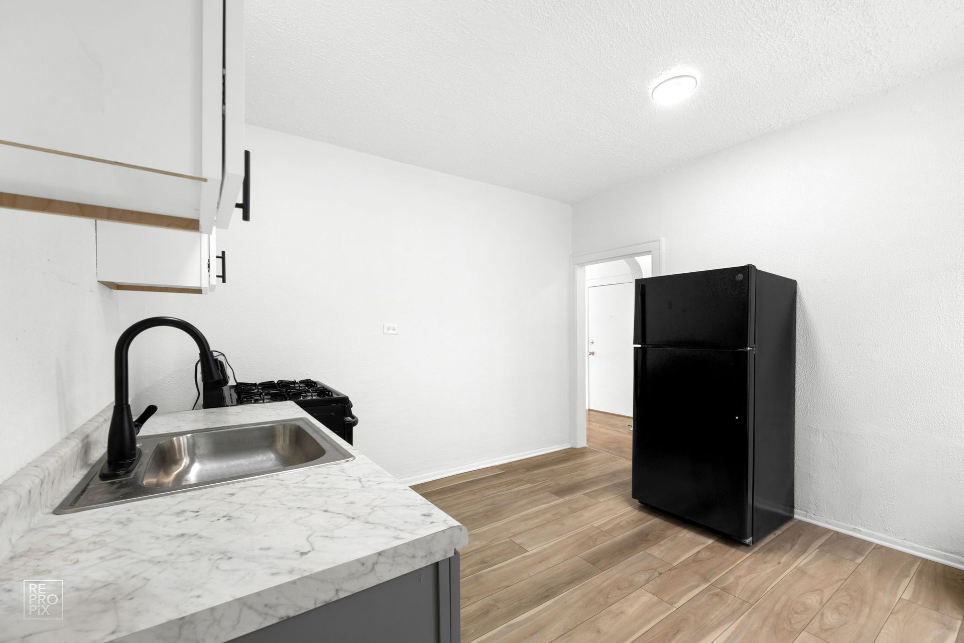 A small kitchen with gray cabinets, marble countertops, black appliances, and light wood flooring.