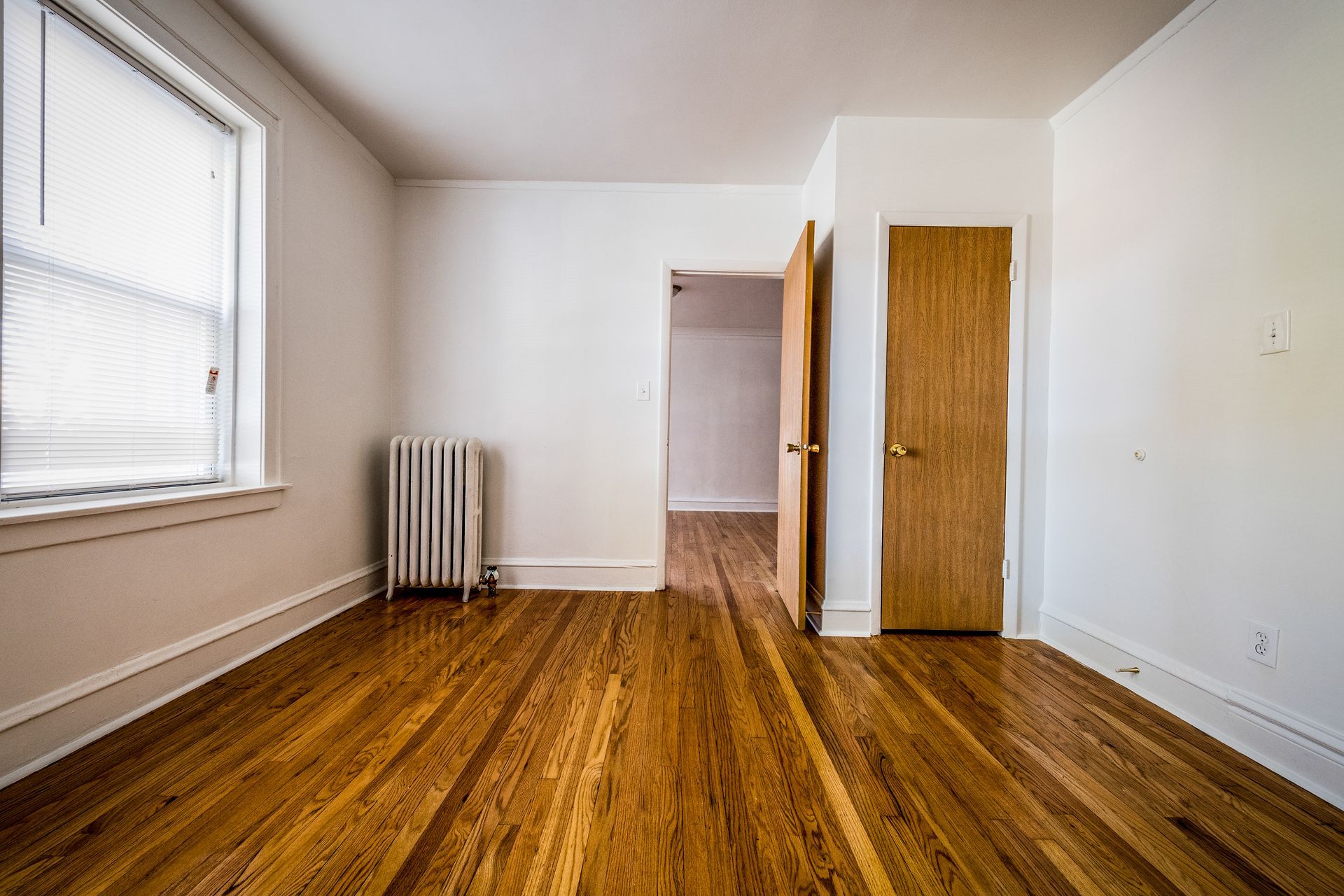 Empty room with hardwood floors, a radiator, window, and two doorways.