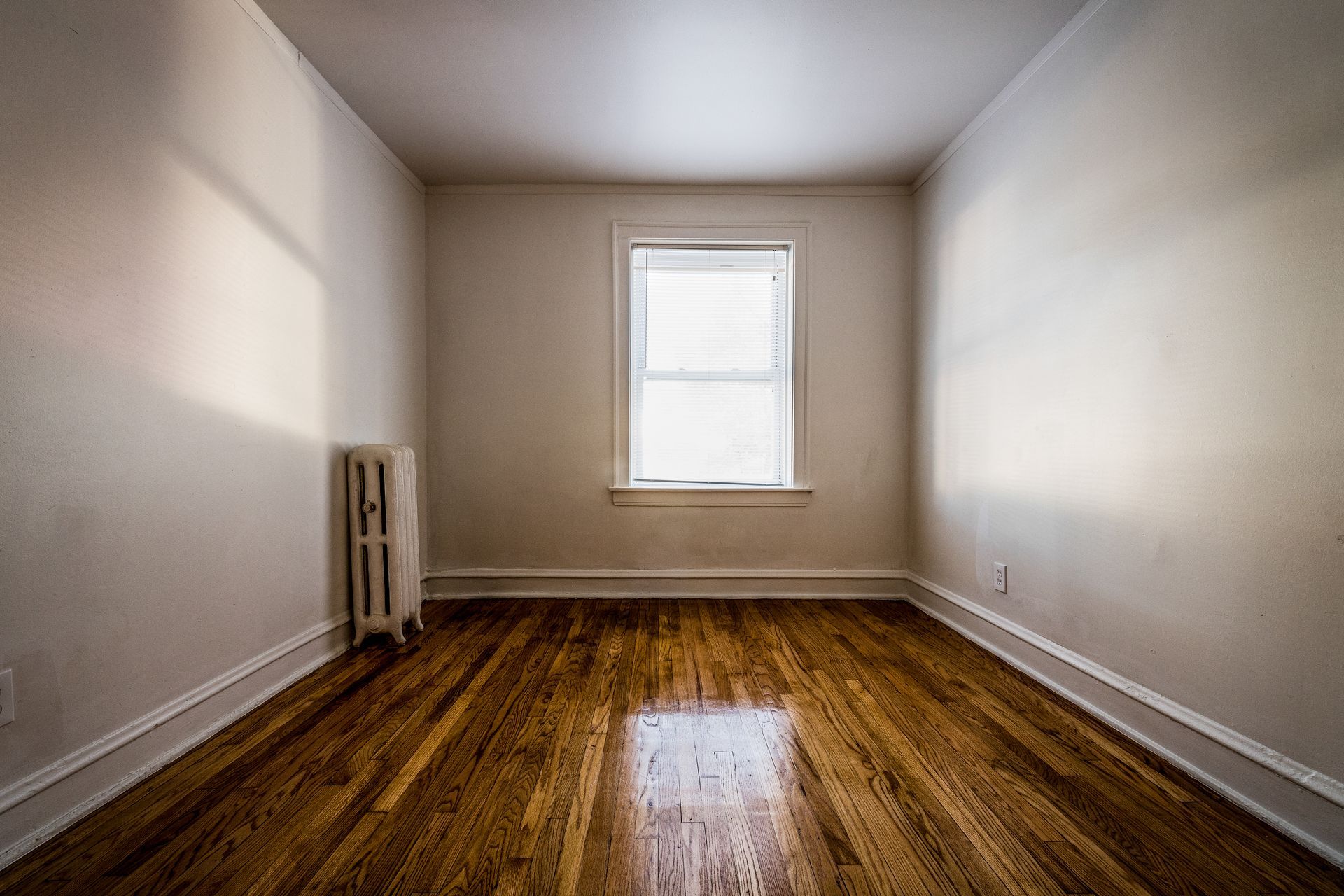 Empty room with hardwood floors, a window, and a radiator on a wall.
