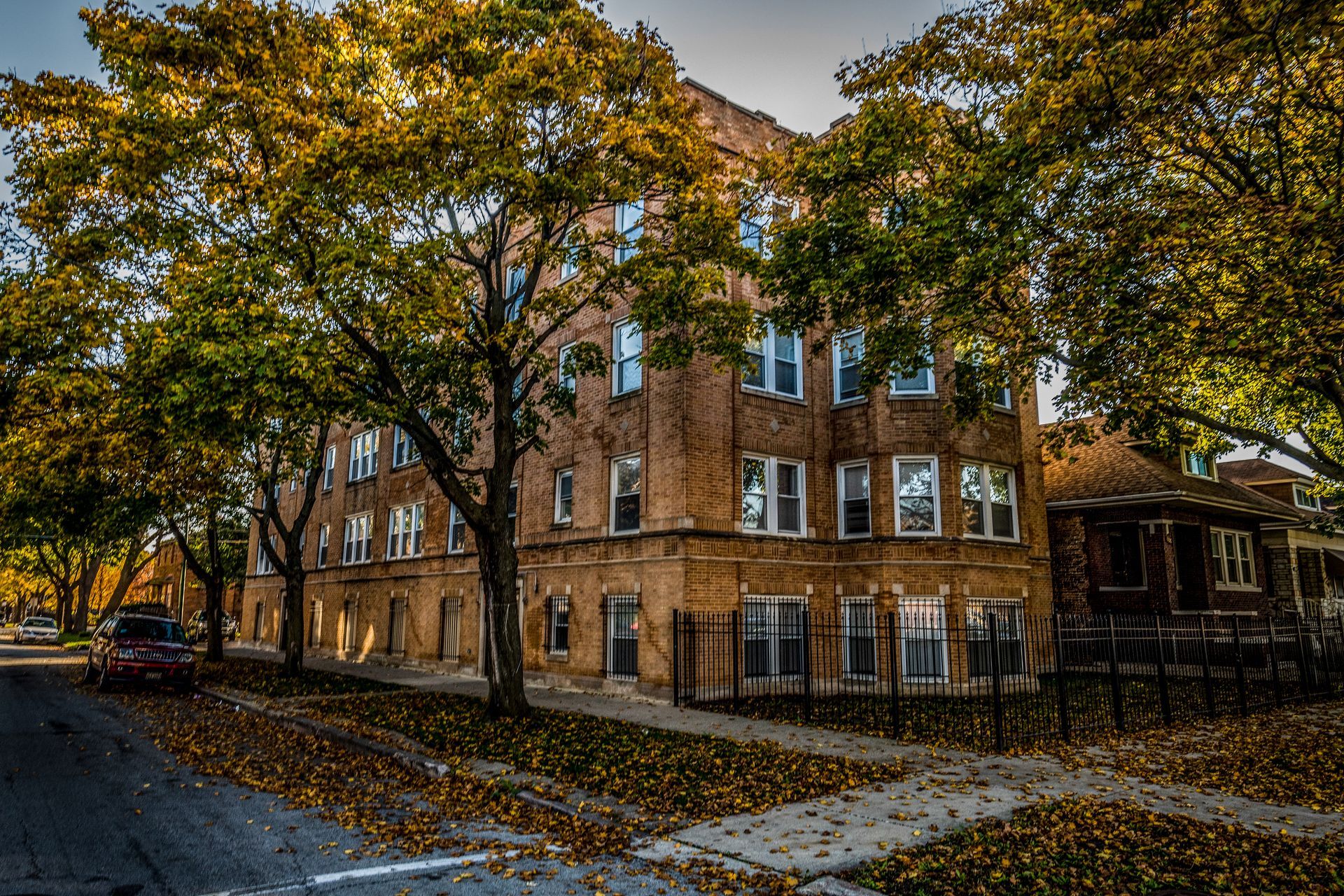 Brick apartment building with autumn leaves, car on street.