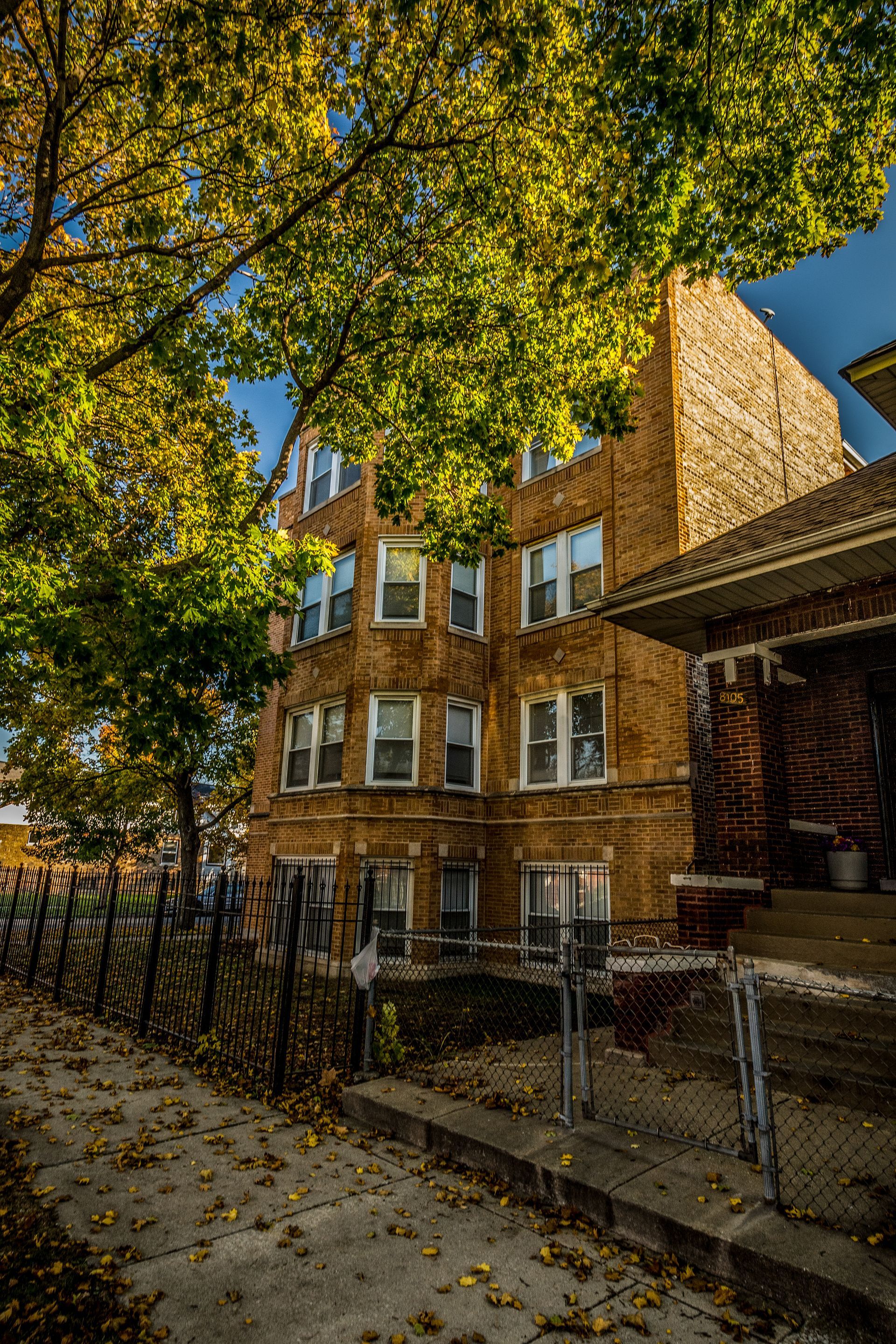 Brick apartment building with autumn leaves, steps leading to entrance.