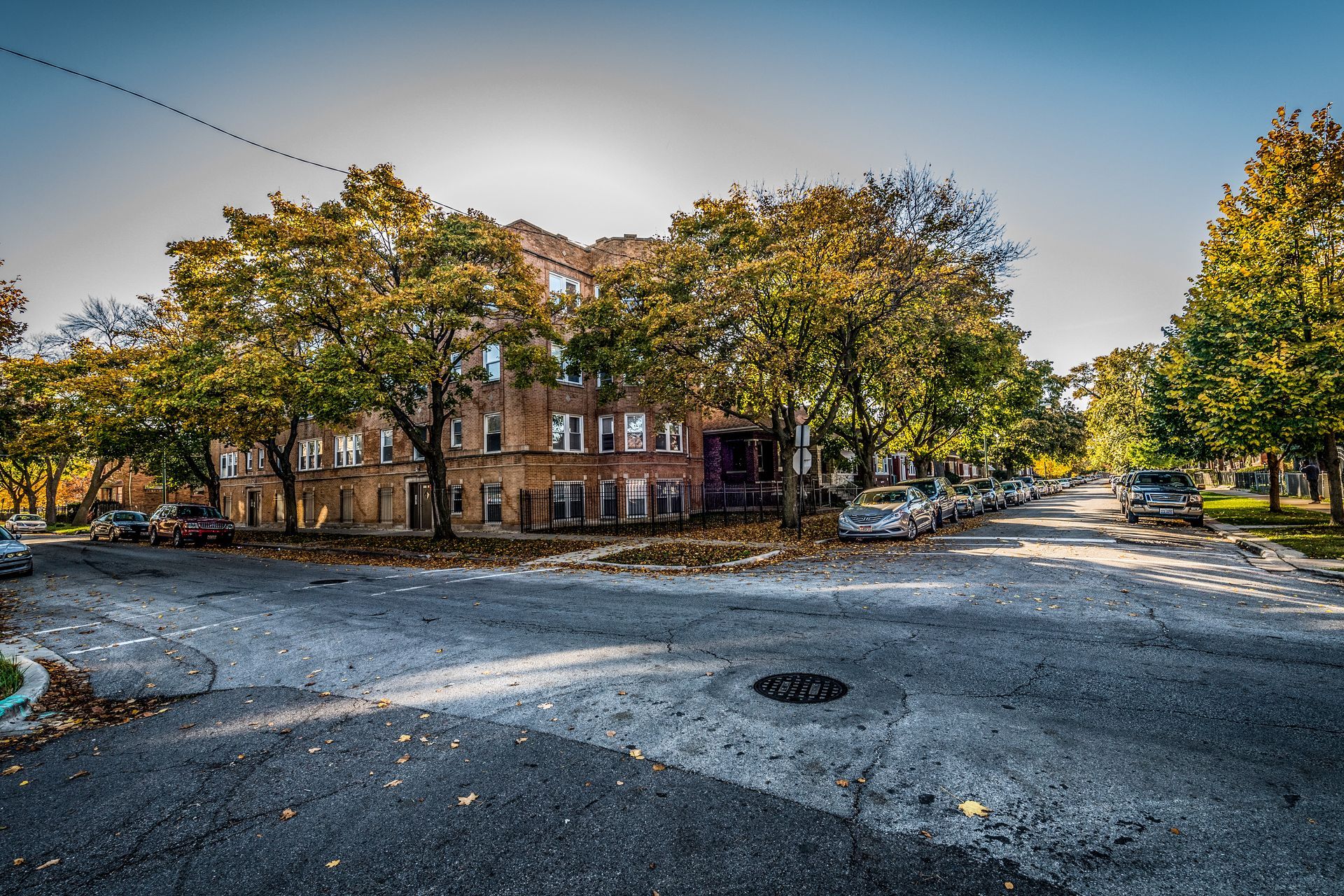 Brick building at a street corner with autumn trees, cars parked along the street.