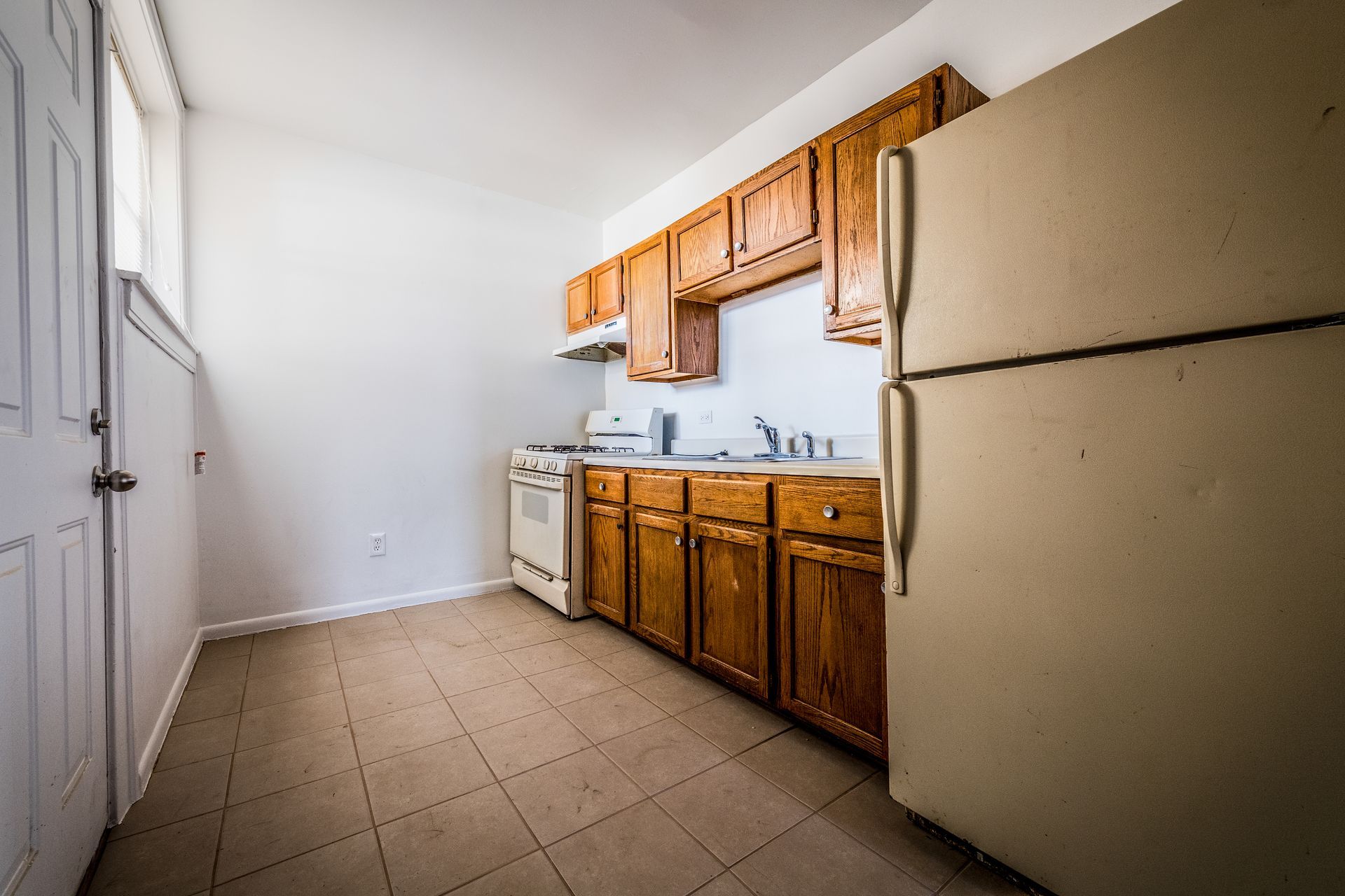 Kitchen with wooden cabinets, a refrigerator, and exposed brick wall.
