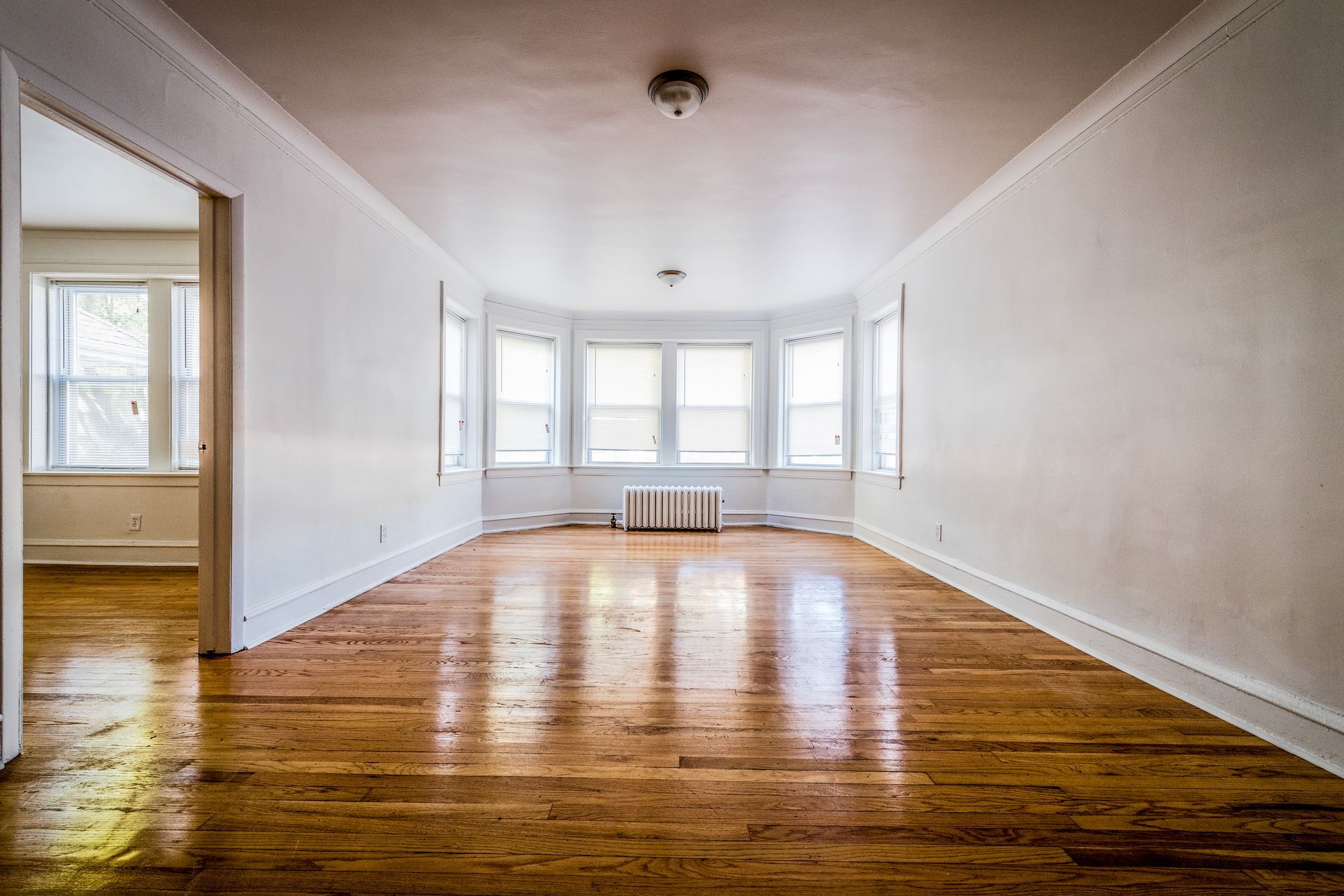 Empty room with hardwood floors, bay windows, and white walls.