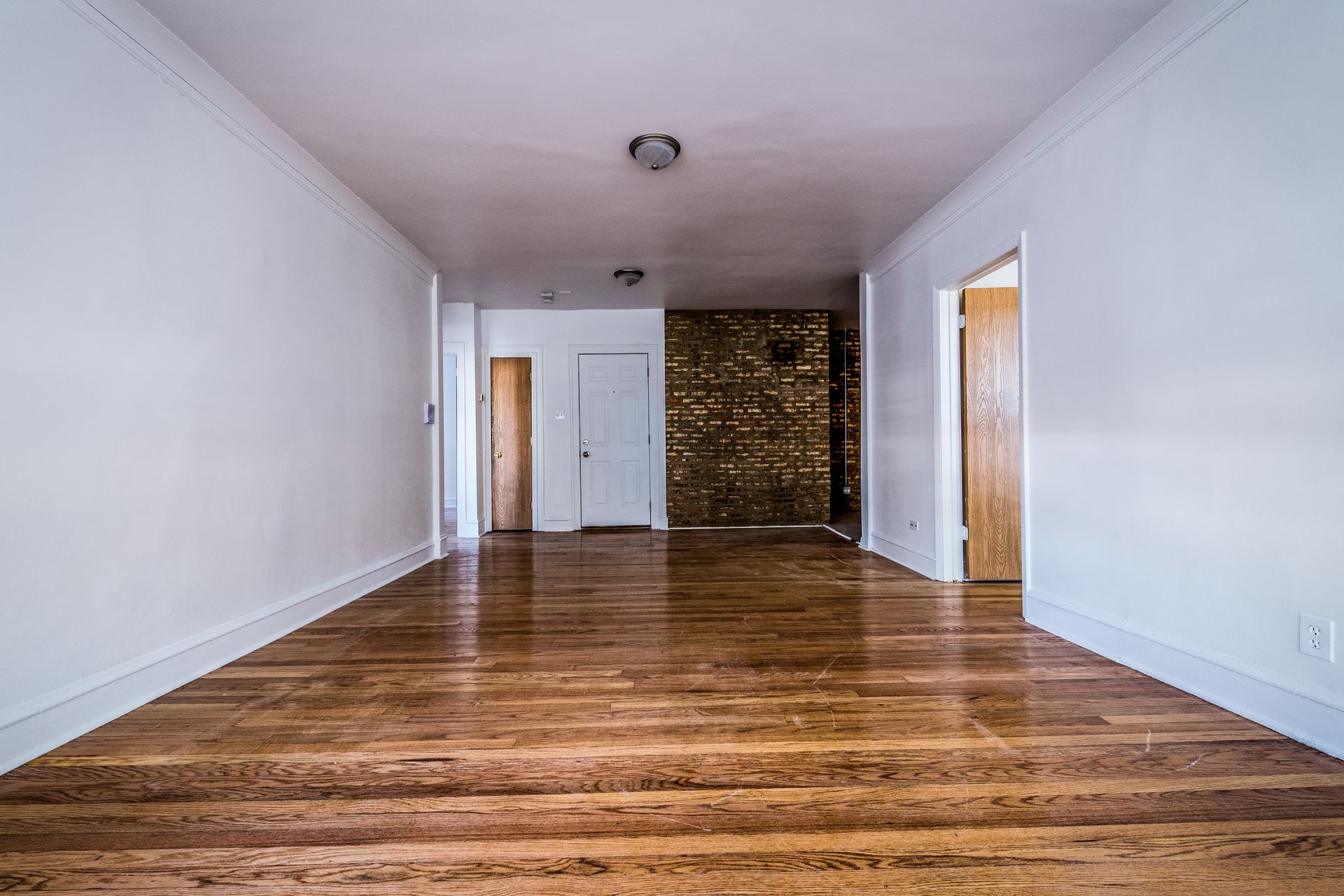 Empty room with hardwood floors, white walls, and doorways leading to other rooms.