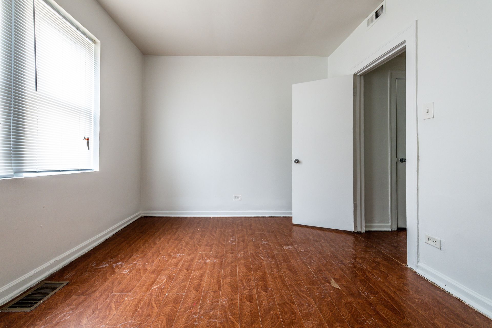 Empty room with wooden floors, white walls, closet, and a large window with blinds.