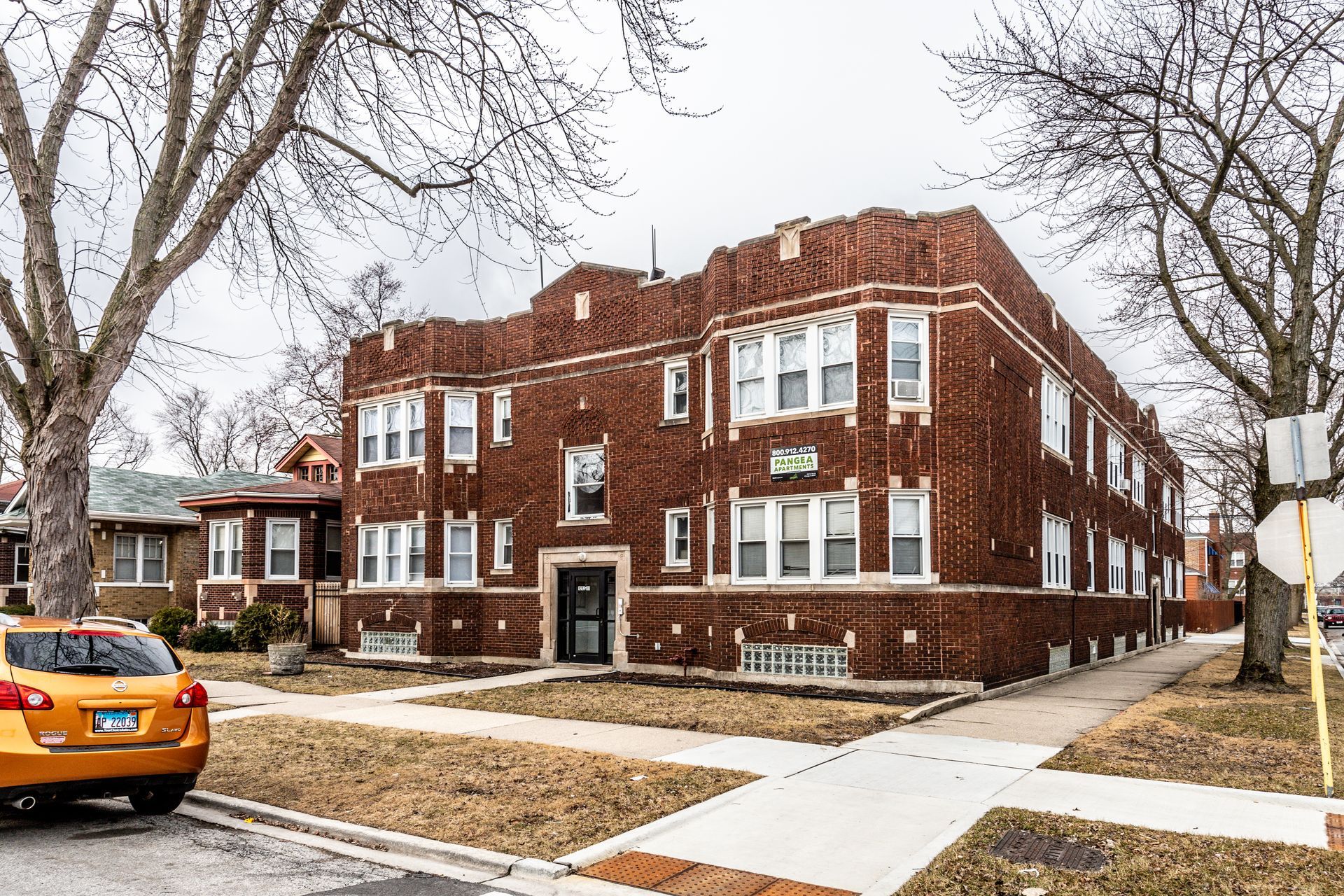 Brick apartment building on a residential street; orange car parked in front. Overcast day.