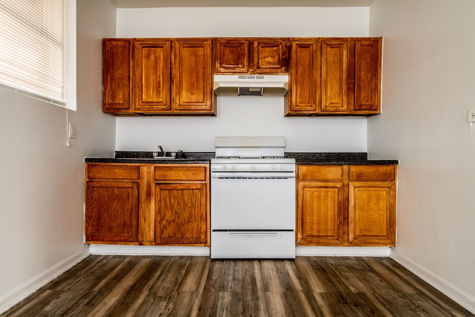 Kitchen with wooden cabinets, white stove, and black countertops; wooden floor.