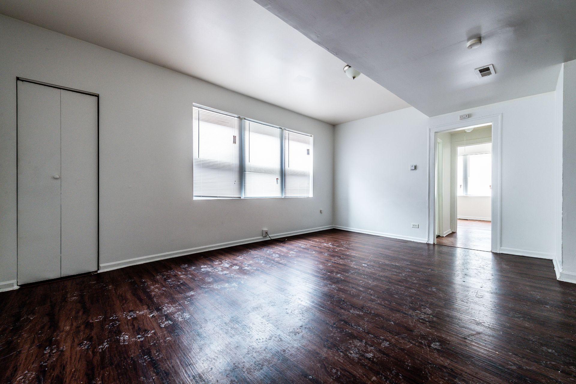 Empty room with dark wood floor, white walls, three windows with shades, and a doorway.