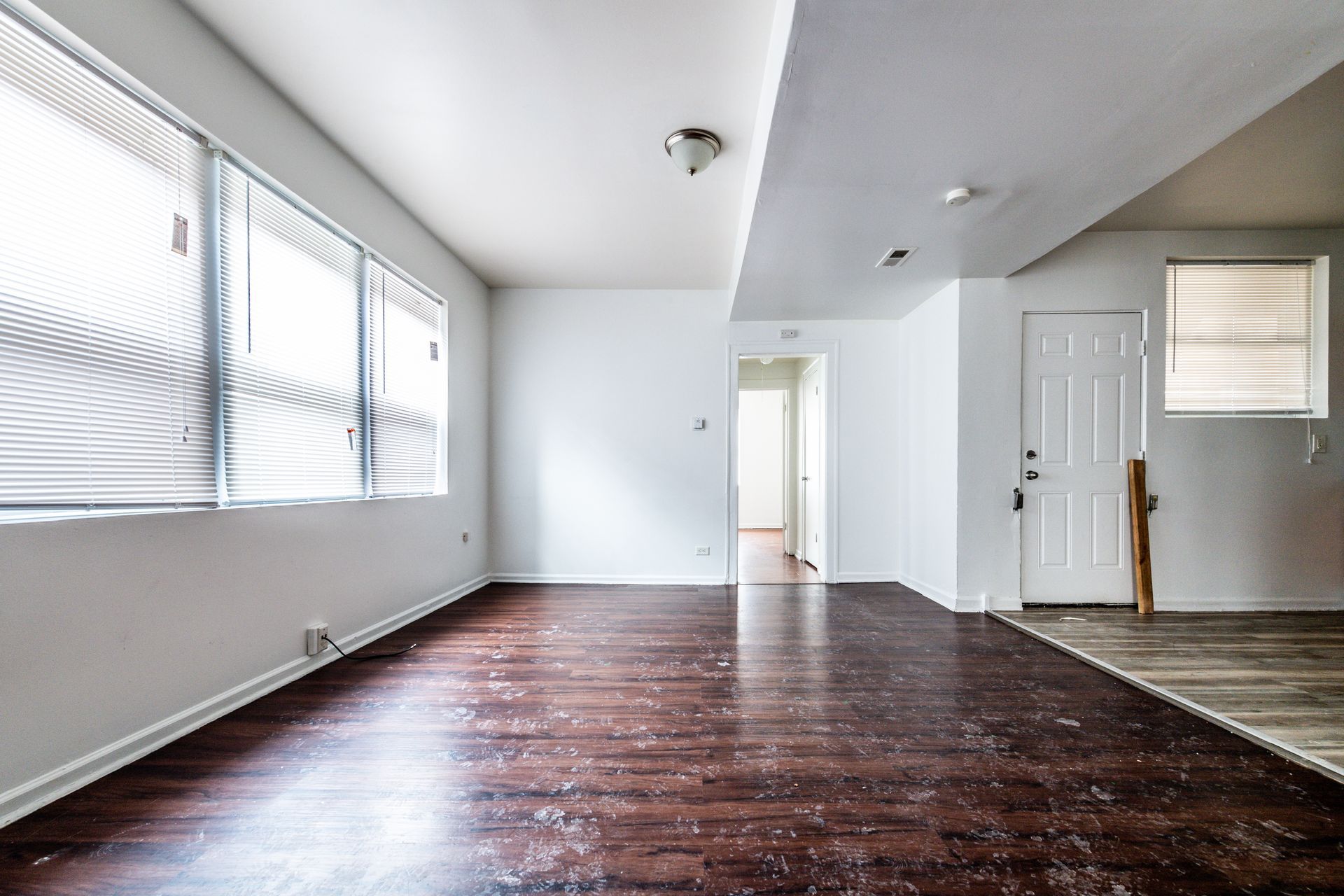 Empty interior of a room with dark wood floors, white walls, and a window.