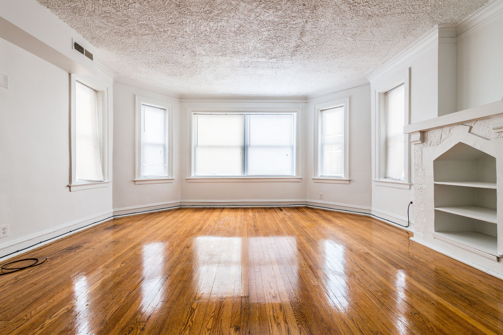 Empty living room with wood floors, bay windows, and a white fireplace.