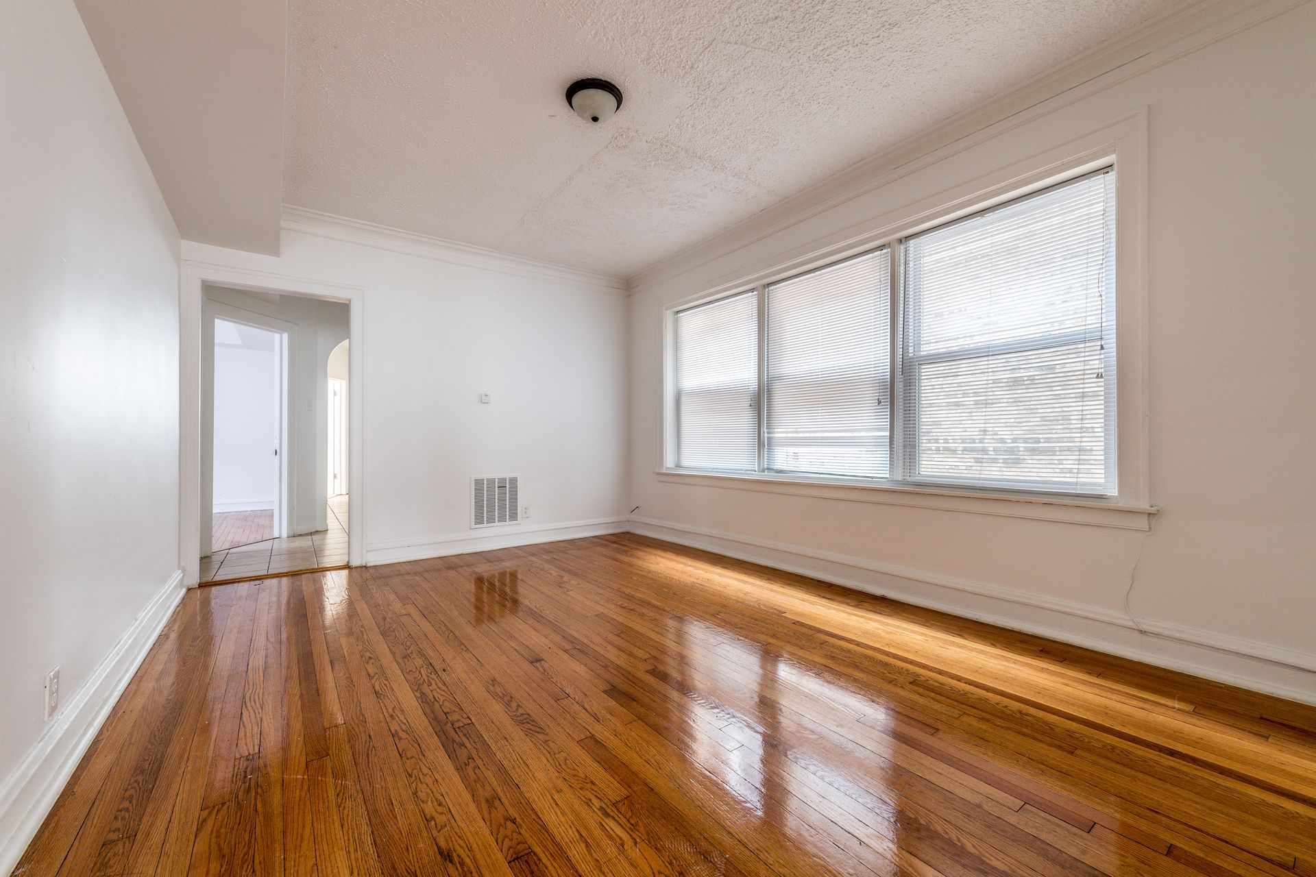 Empty room with wood flooring, white walls, and a large window with blinds.