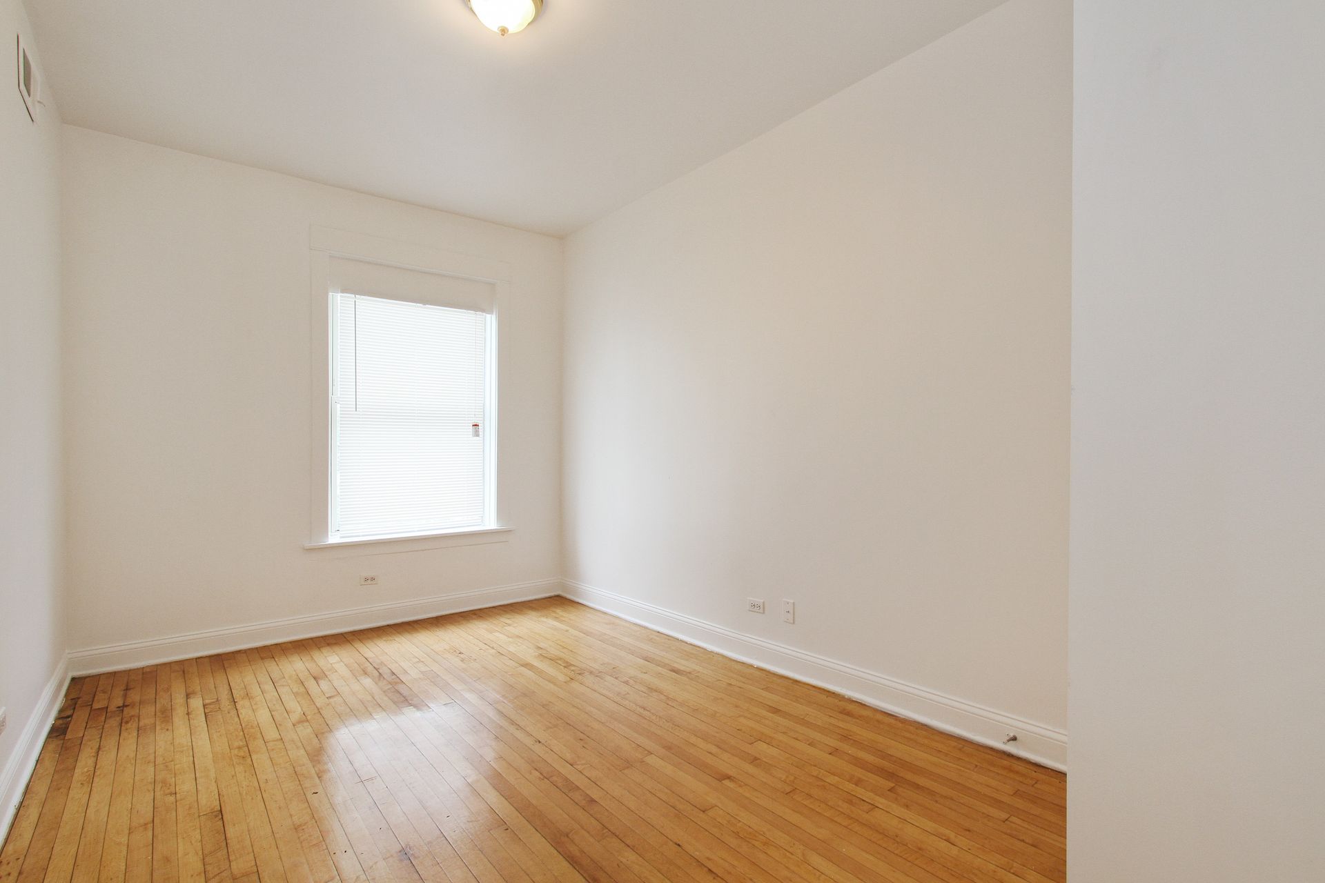 Empty room with hardwood floors, white walls, and a small window with blinds.