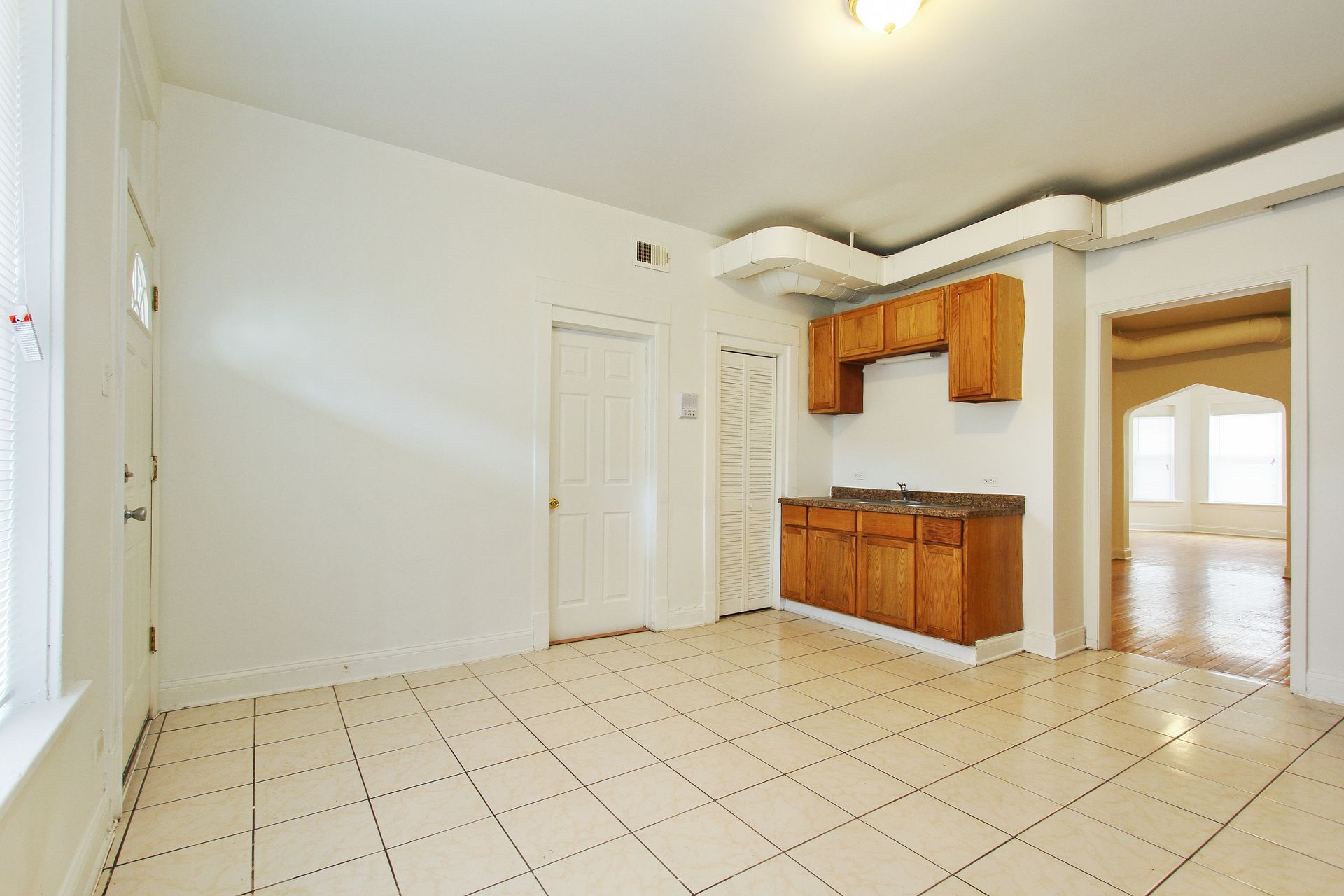 Empty apartment interior with tile floor, partial kitchen, and arched doorway.