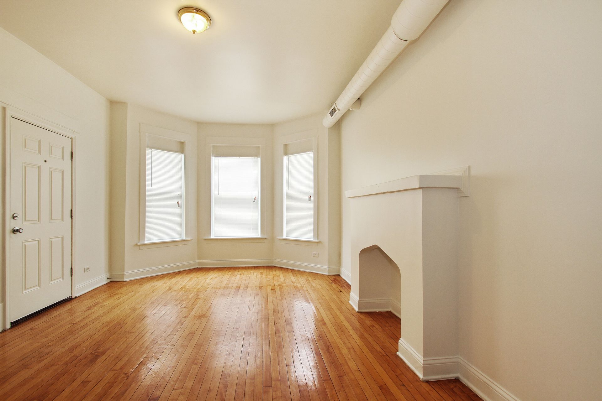 Empty room with hardwood floors, bay windows, and a white fireplace.