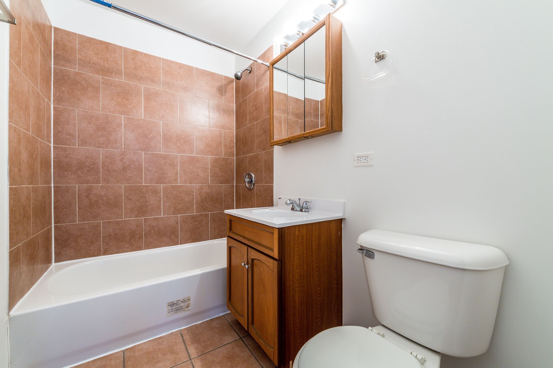 Bathroom with brown tiled wall, white tub, vanity, and toilet.