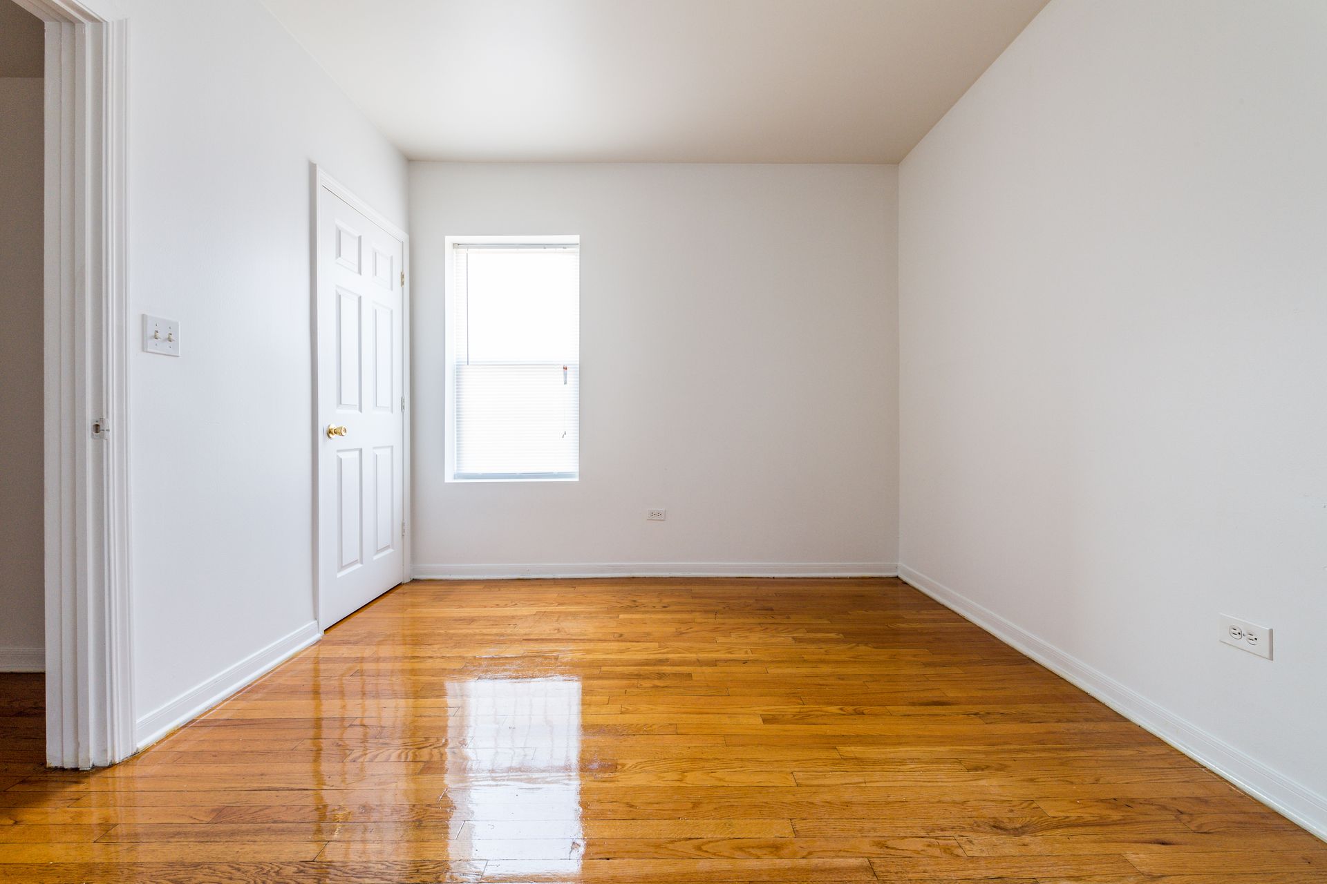 Empty room with hardwood floors, white walls, and a window.