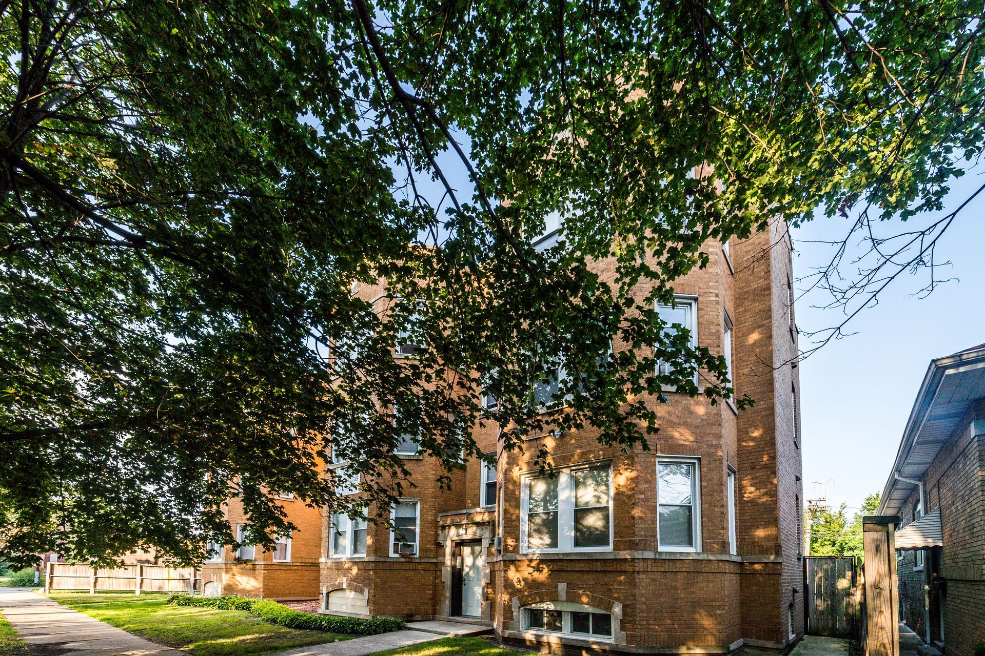 Brick apartment building under a leafy tree, with windows and a side entrance.