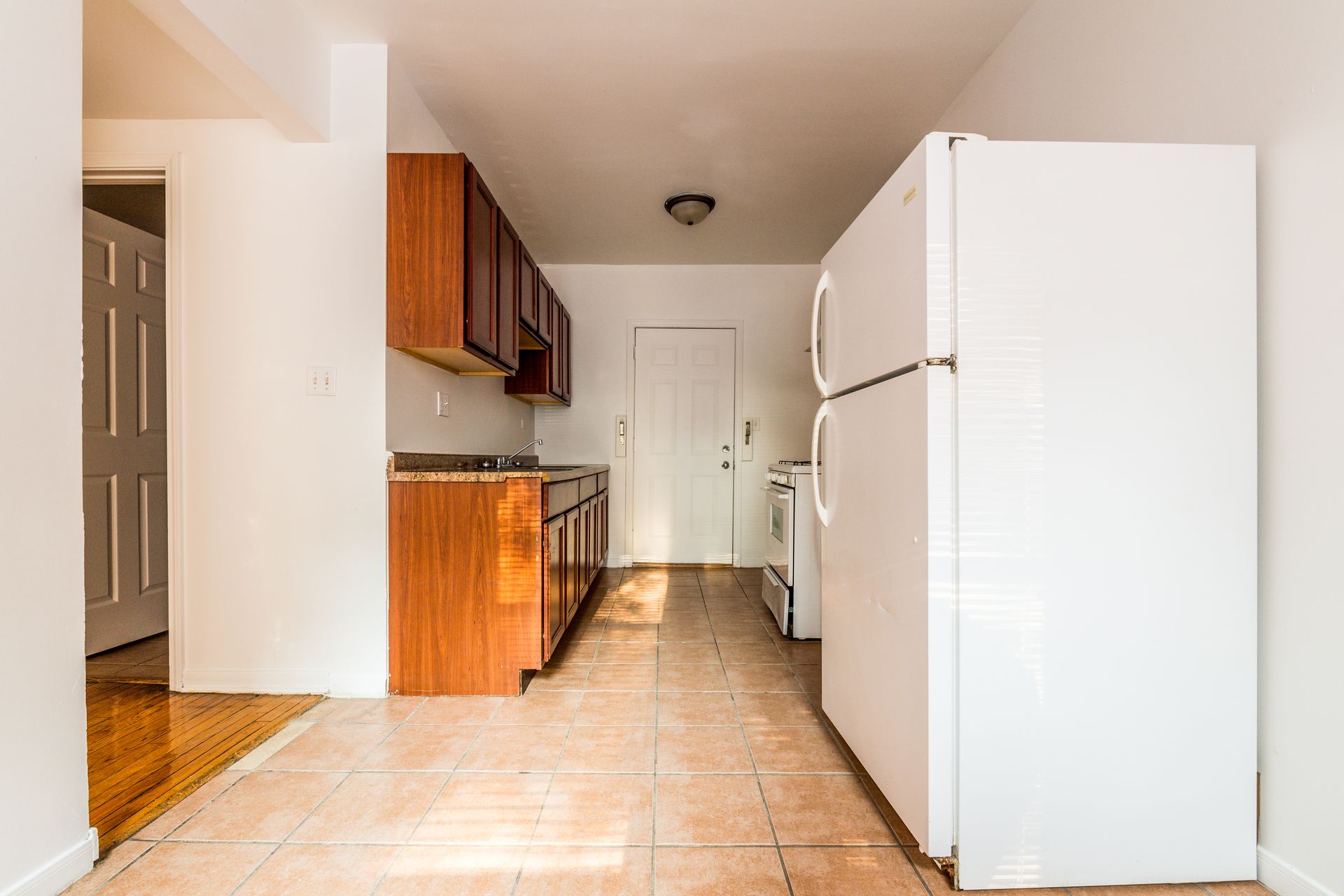 Empty kitchen with wood cabinets, white appliances, and tiled floor.