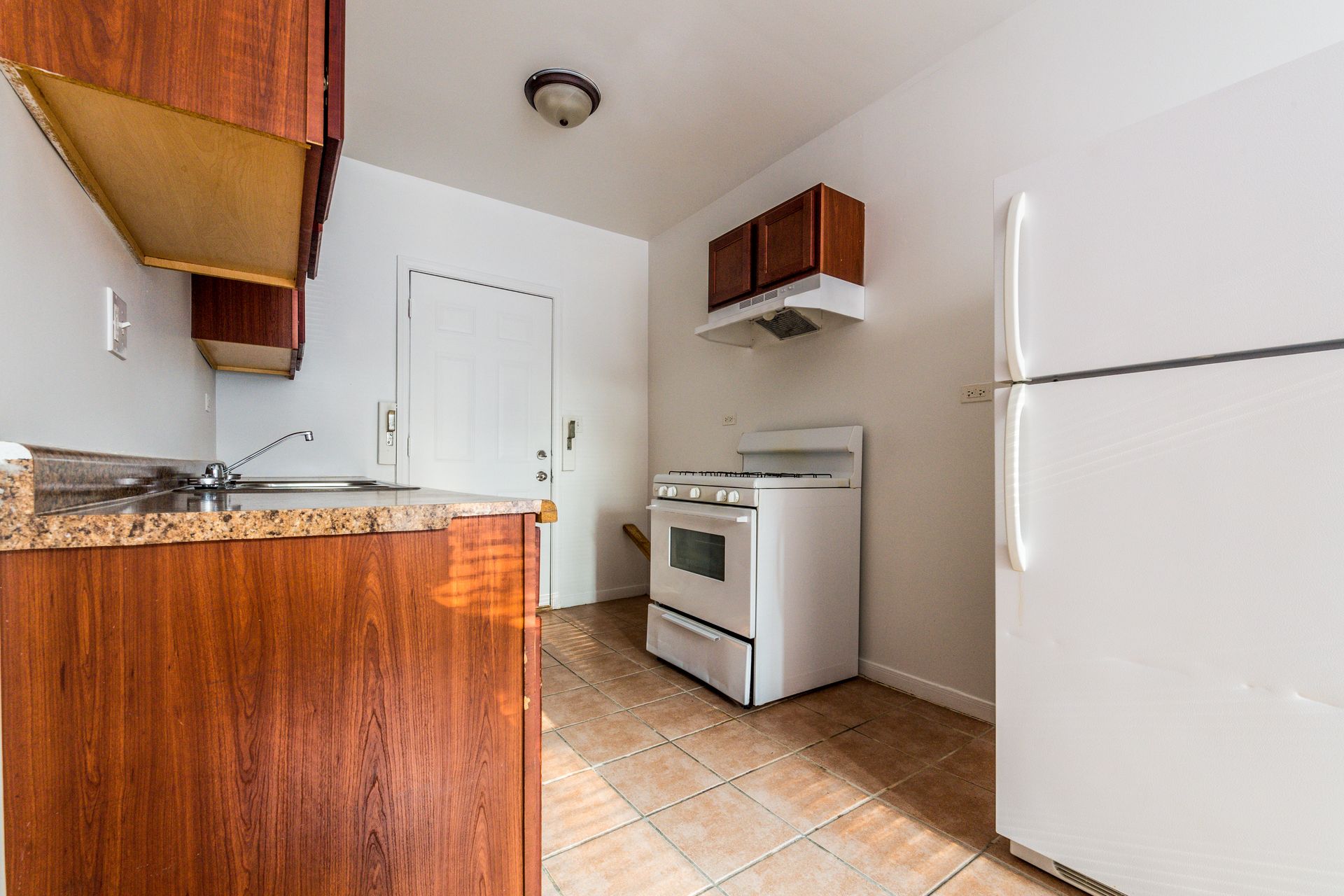 A small kitchen with wood cabinets, white appliances, and a tile floor.