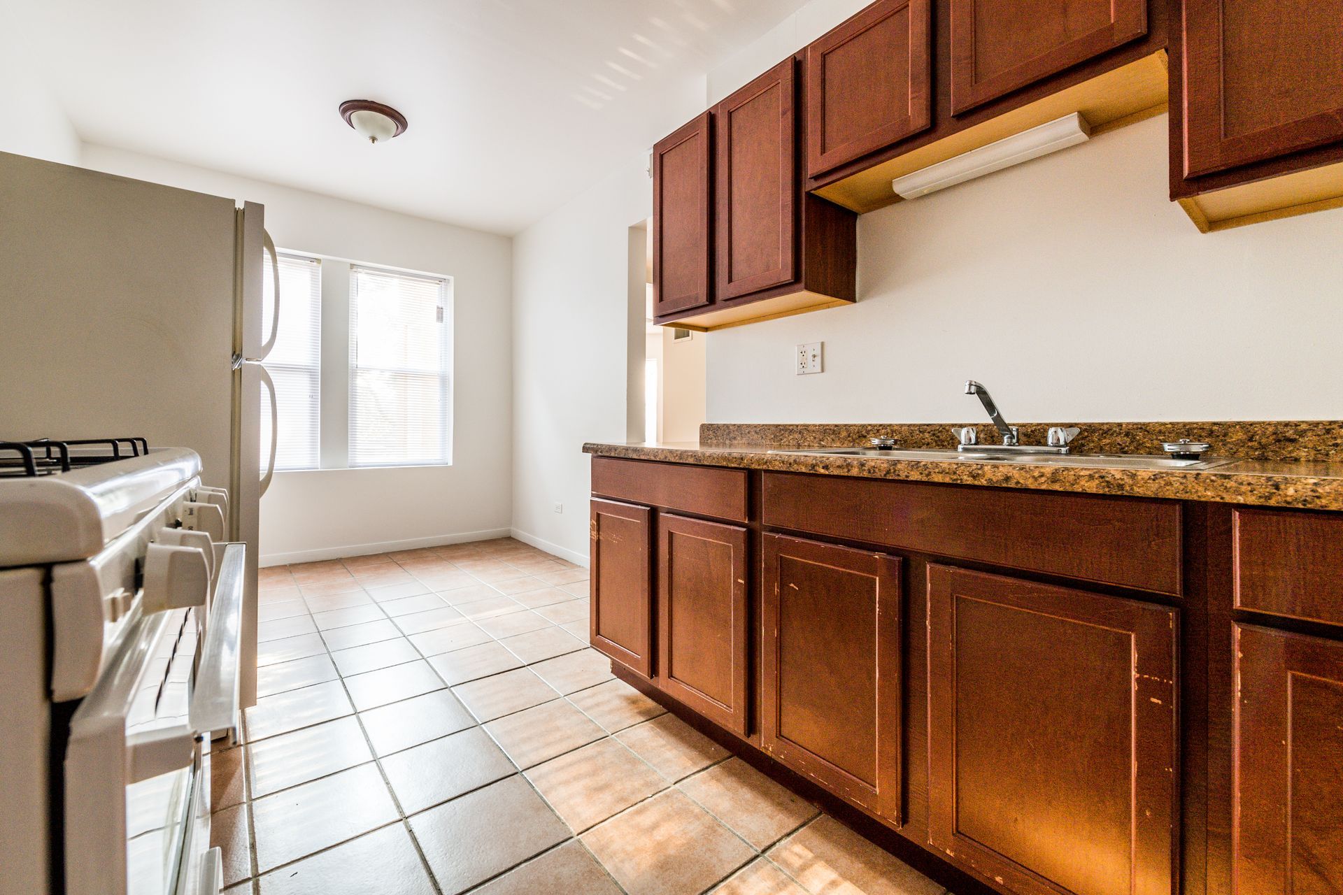 Empty kitchen with white appliances, dark cabinets, and tile floor.