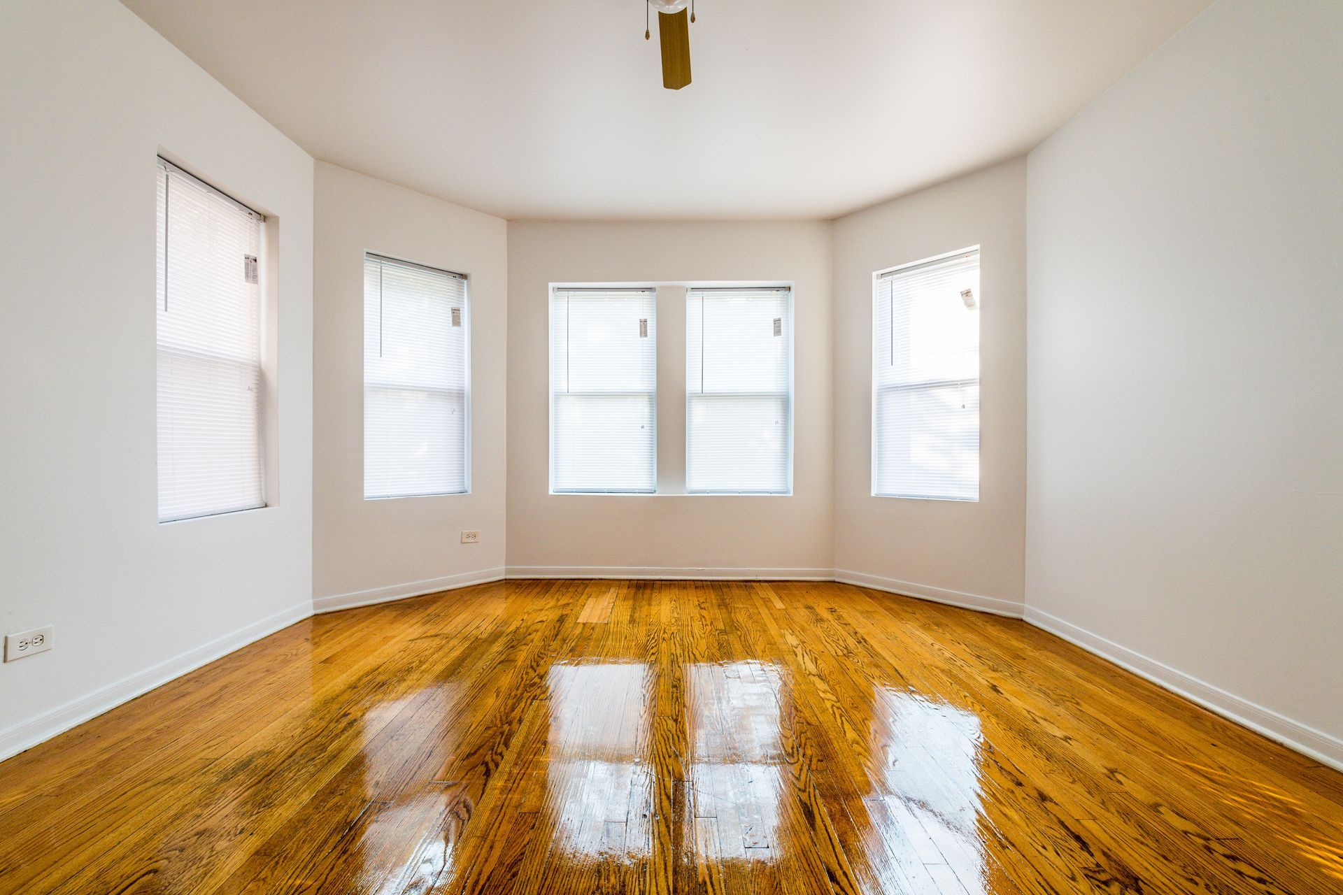 Empty room with hardwood floors, white walls, and a bay window.