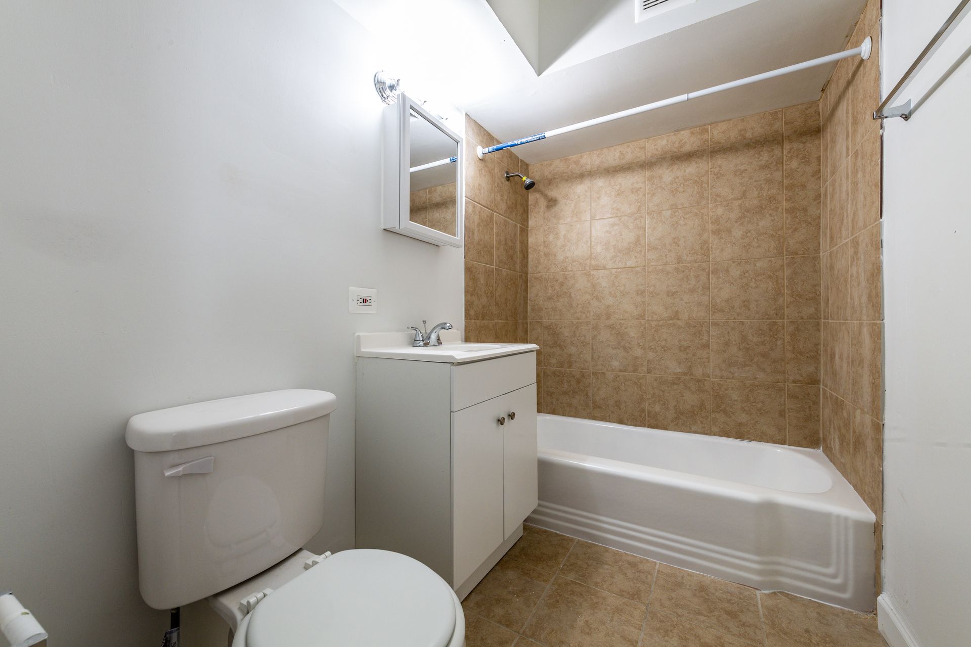 Bathroom with a white toilet, vanity, and bathtub with a brown tile surround.