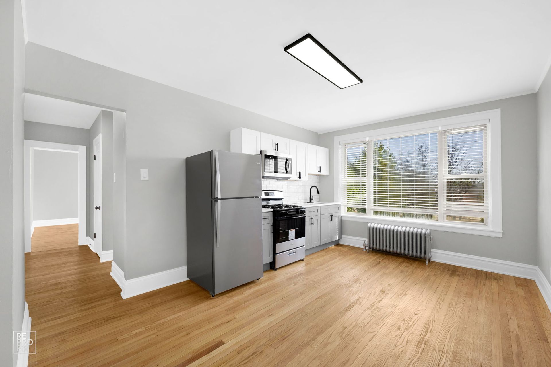 Kitchen with stainless steel appliances, white cabinets, and large window overlooking trees.