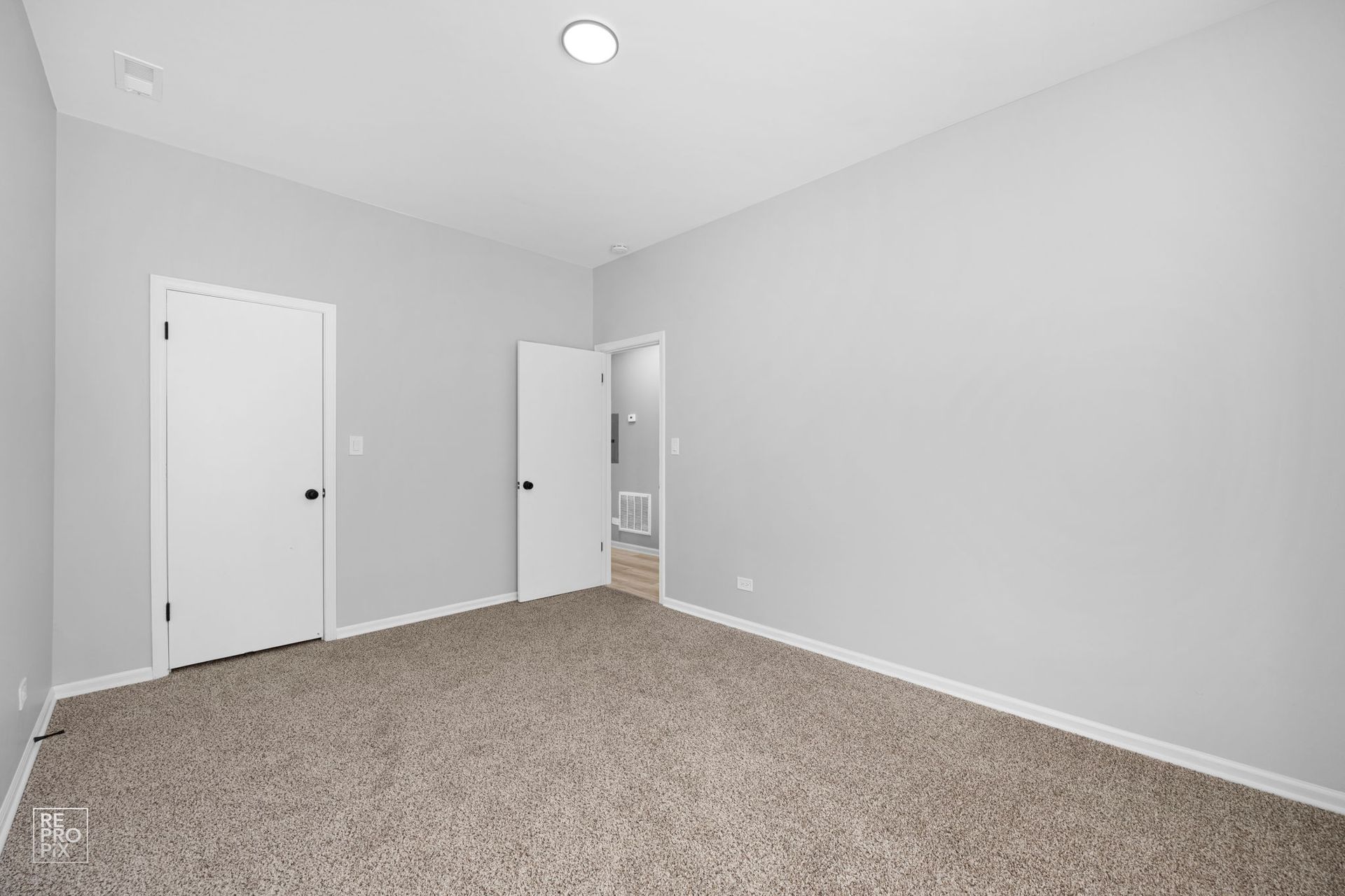 Empty bedroom with light gray walls, two white doors, and beige carpet.