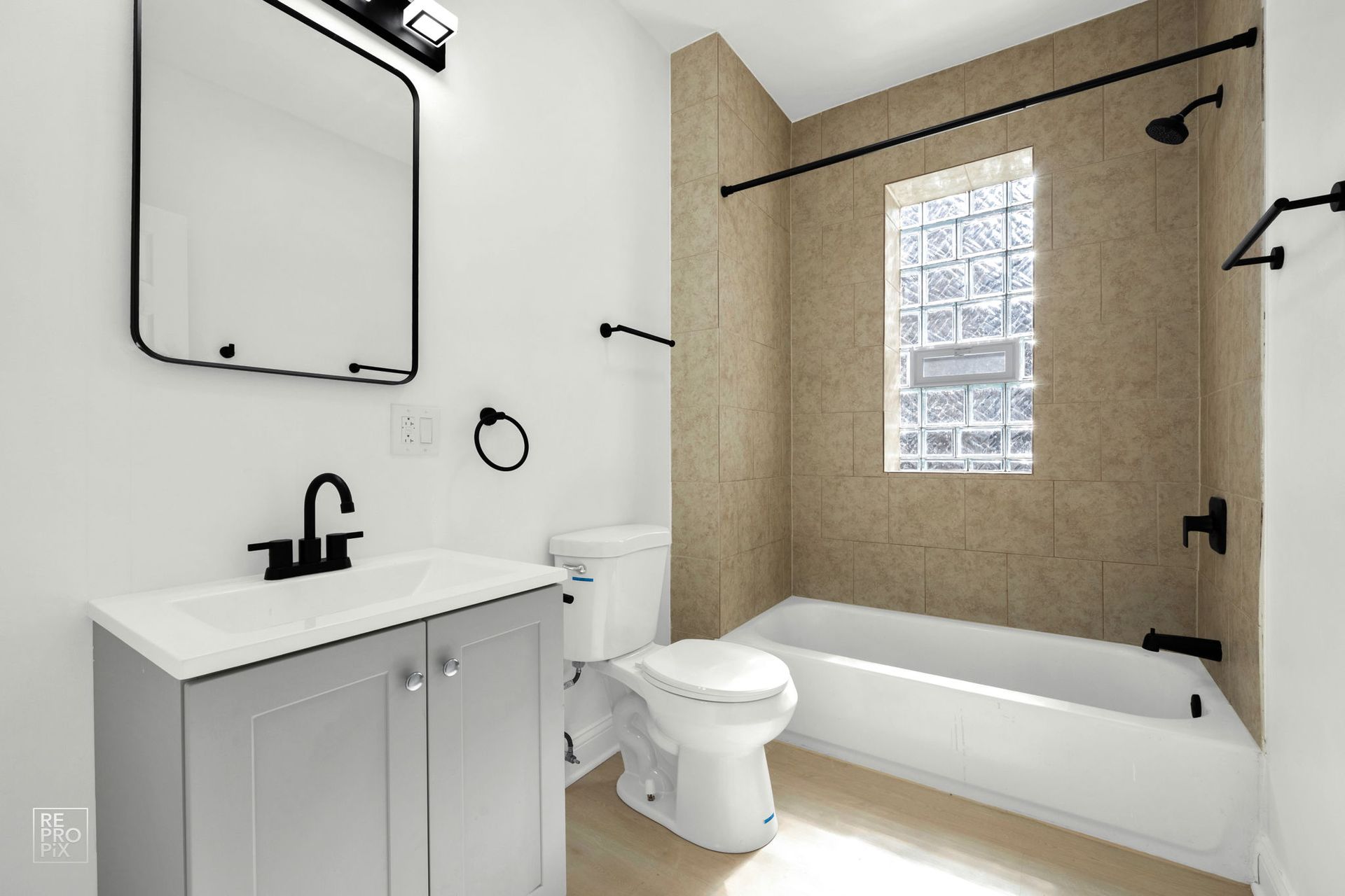 Bathroom with gray vanity, white toilet, and beige shower wall, black fixtures, and mirror.
