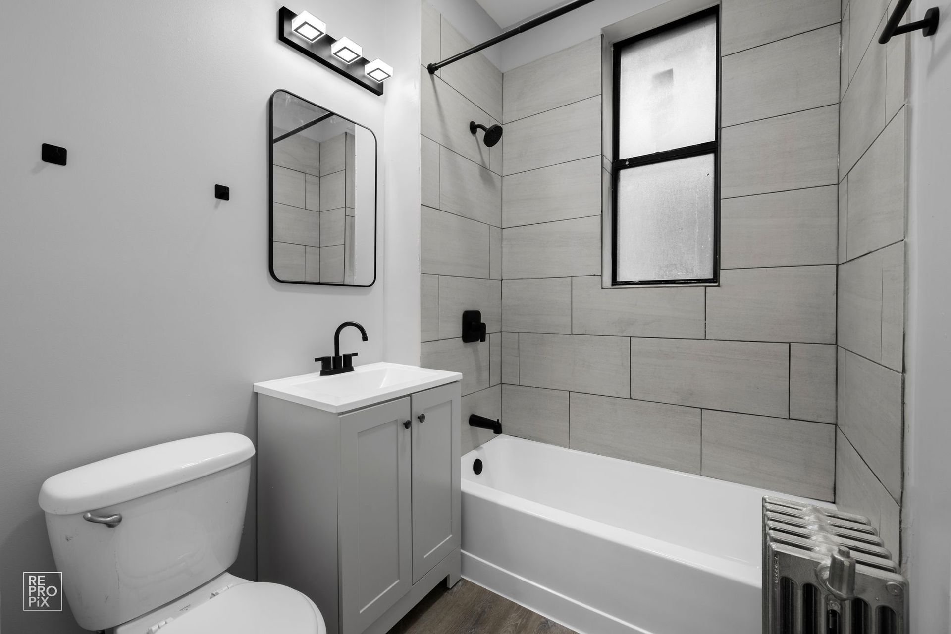Small, modern bathroom with white tile and fixtures, black accents, and a window.