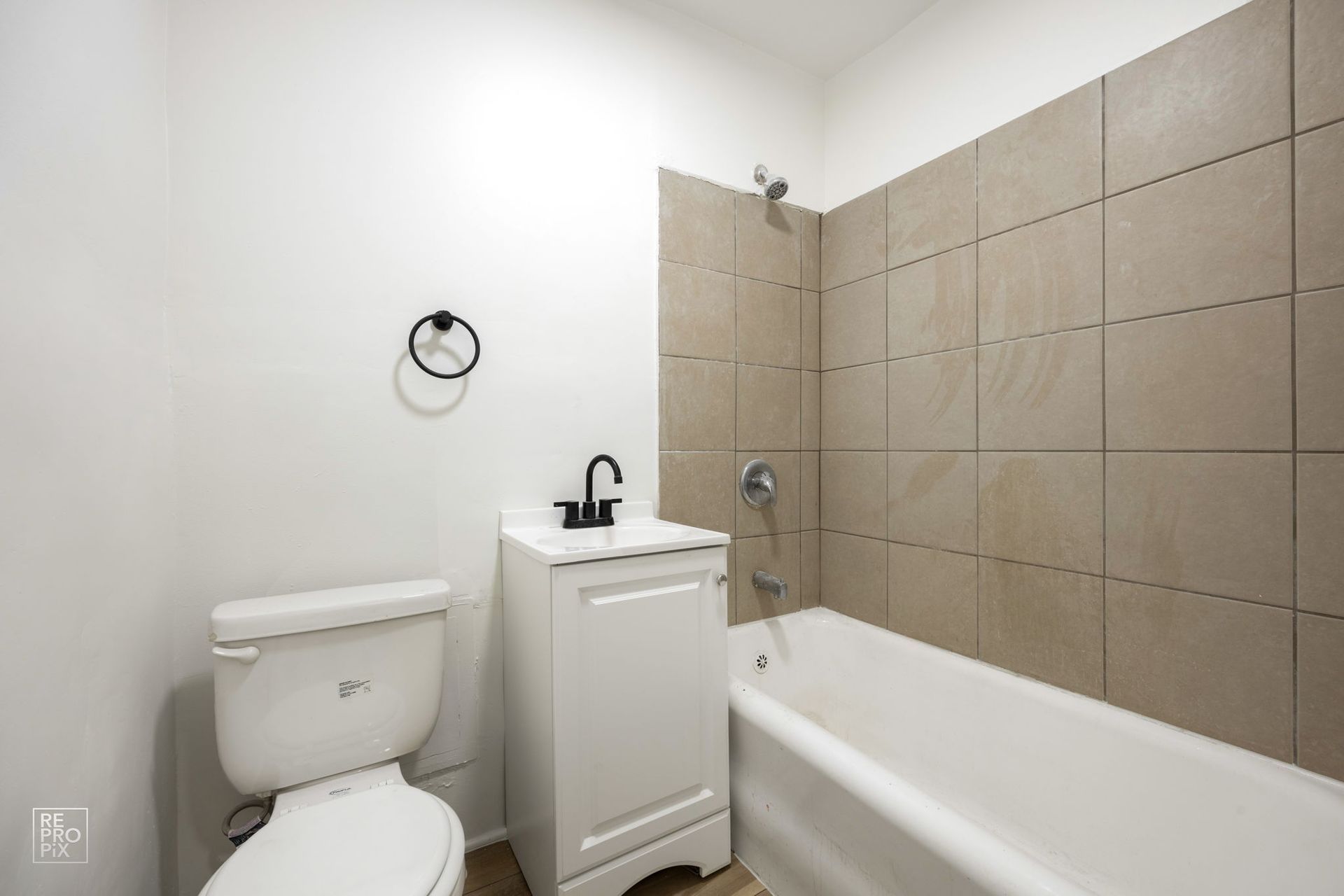 Bathroom with white toilet, vanity, and bathtub, beige tiled wall, black fixtures.