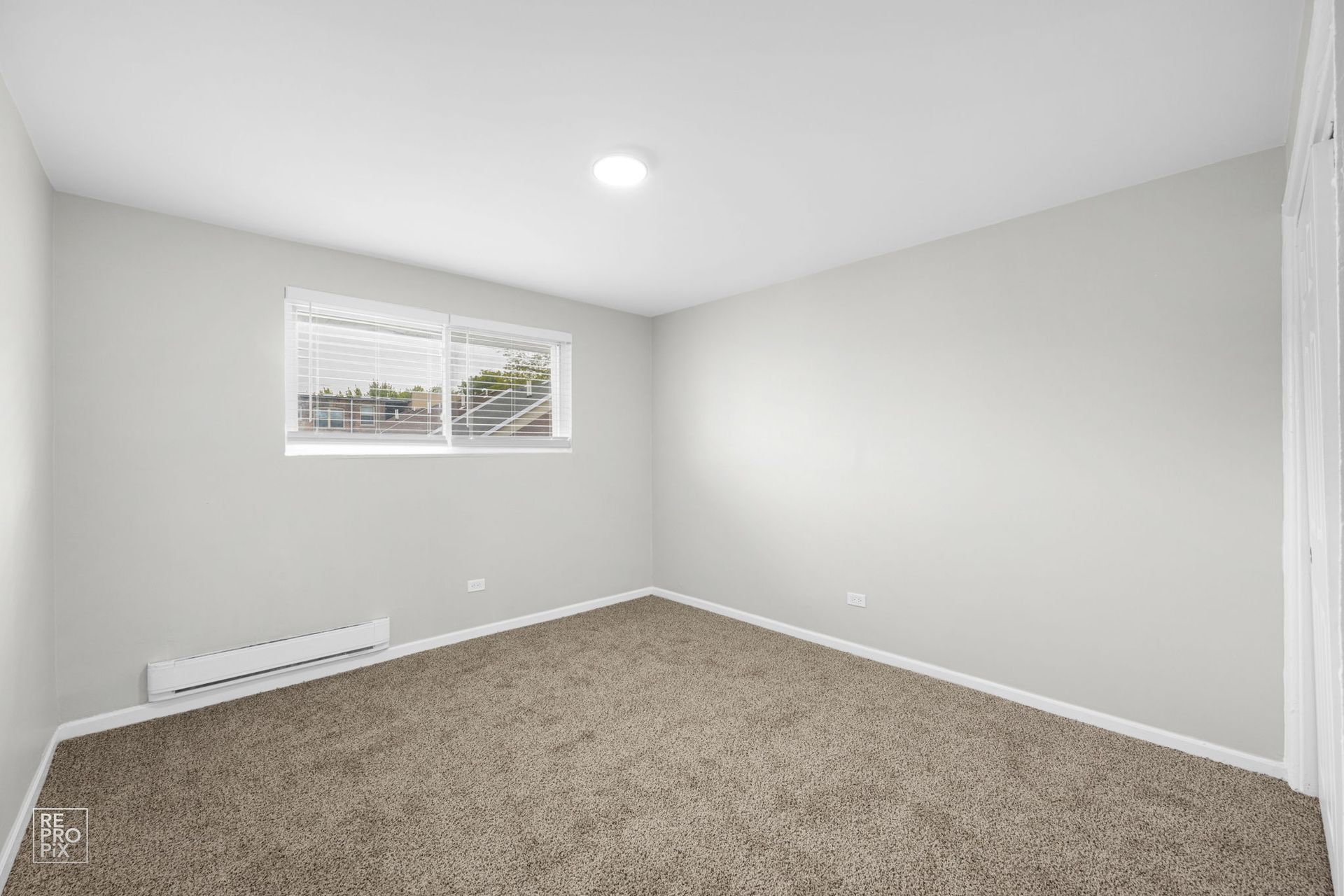 Empty bedroom with beige carpet, window, and white walls.