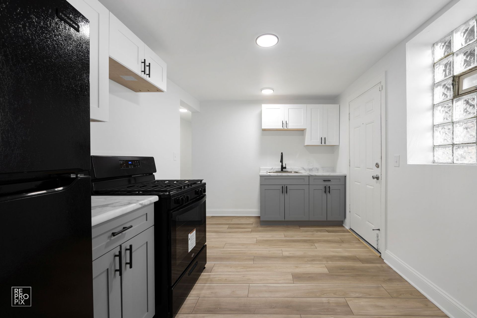 Kitchen with black appliances, white cabinets, and gray lower cabinets; wood-look floor.
