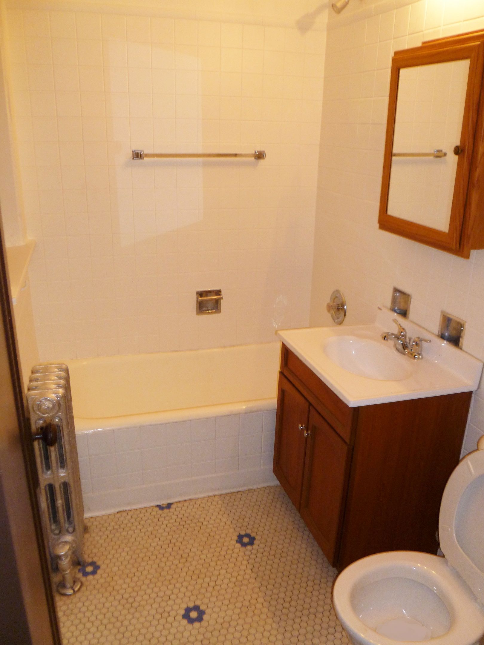 Small bathroom with a tub, sink, toilet, and a medicine cabinet; light-colored tile and flooring.