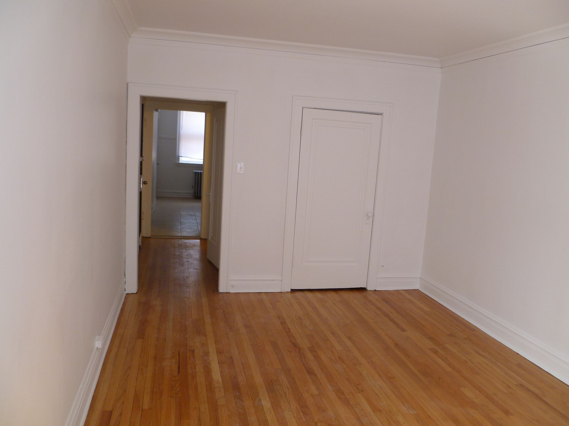 Empty room with hardwood floors, white walls, closet door, and doorway to another room.